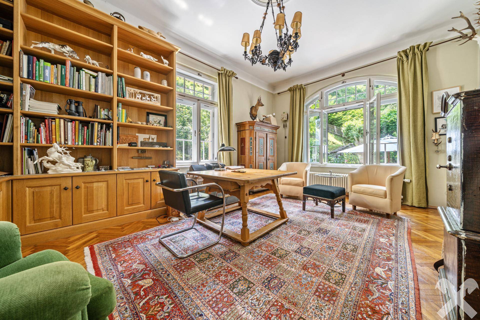 Helles Arbeitszimmer mit großer Holzbibliothek, Schreibtisch und Blick ins Grüne.