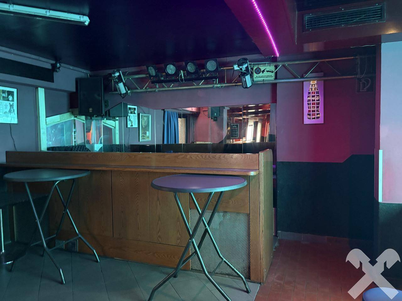Bar mit Holztresen, Stehtischen und Beleuchtungselementen für eine gesellige Atmosphäre.