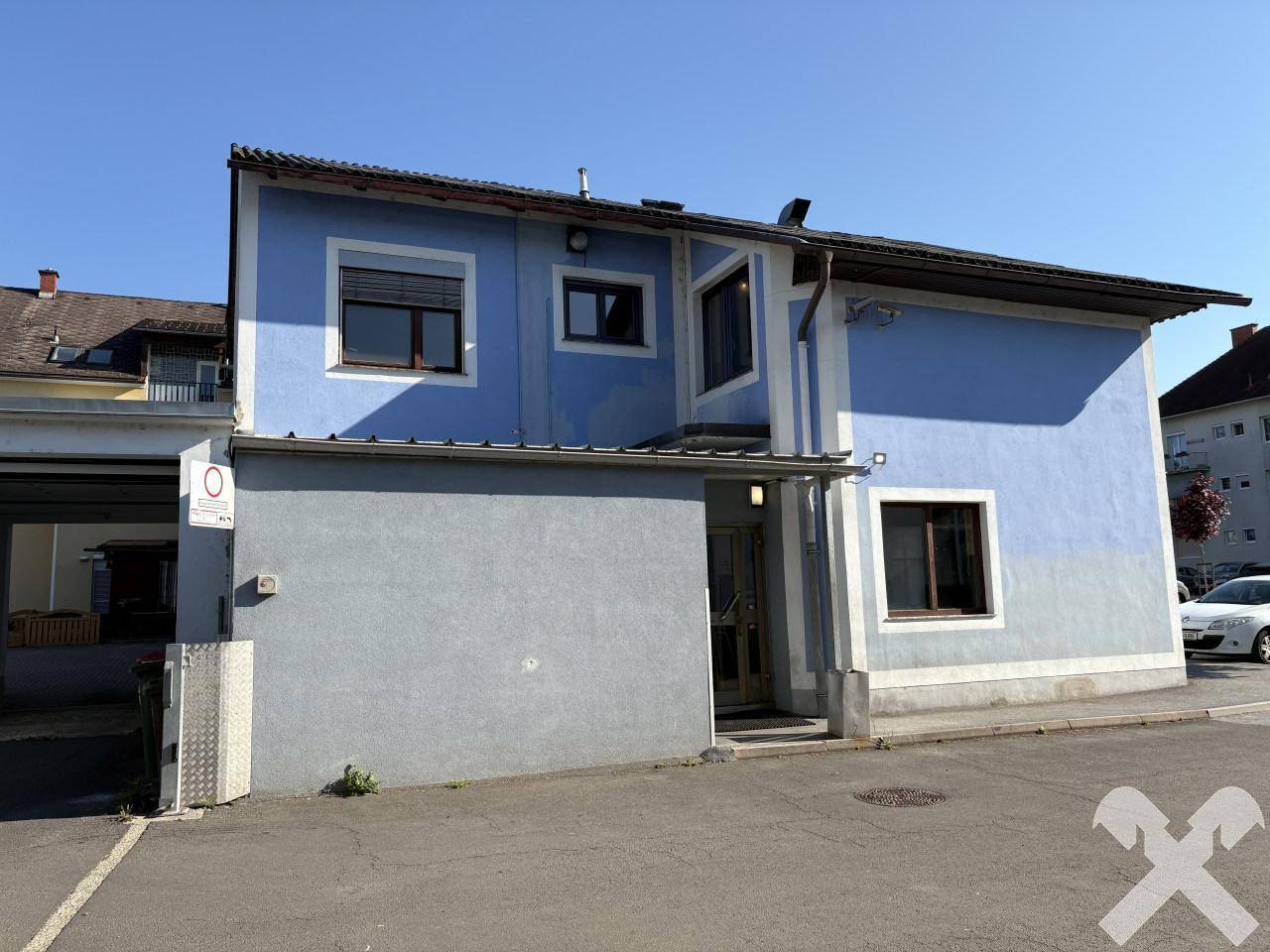 Seitenansicht des Gebäudes mit blauer Fassade und einem grauen Sockelbereich sowie Fenstern.