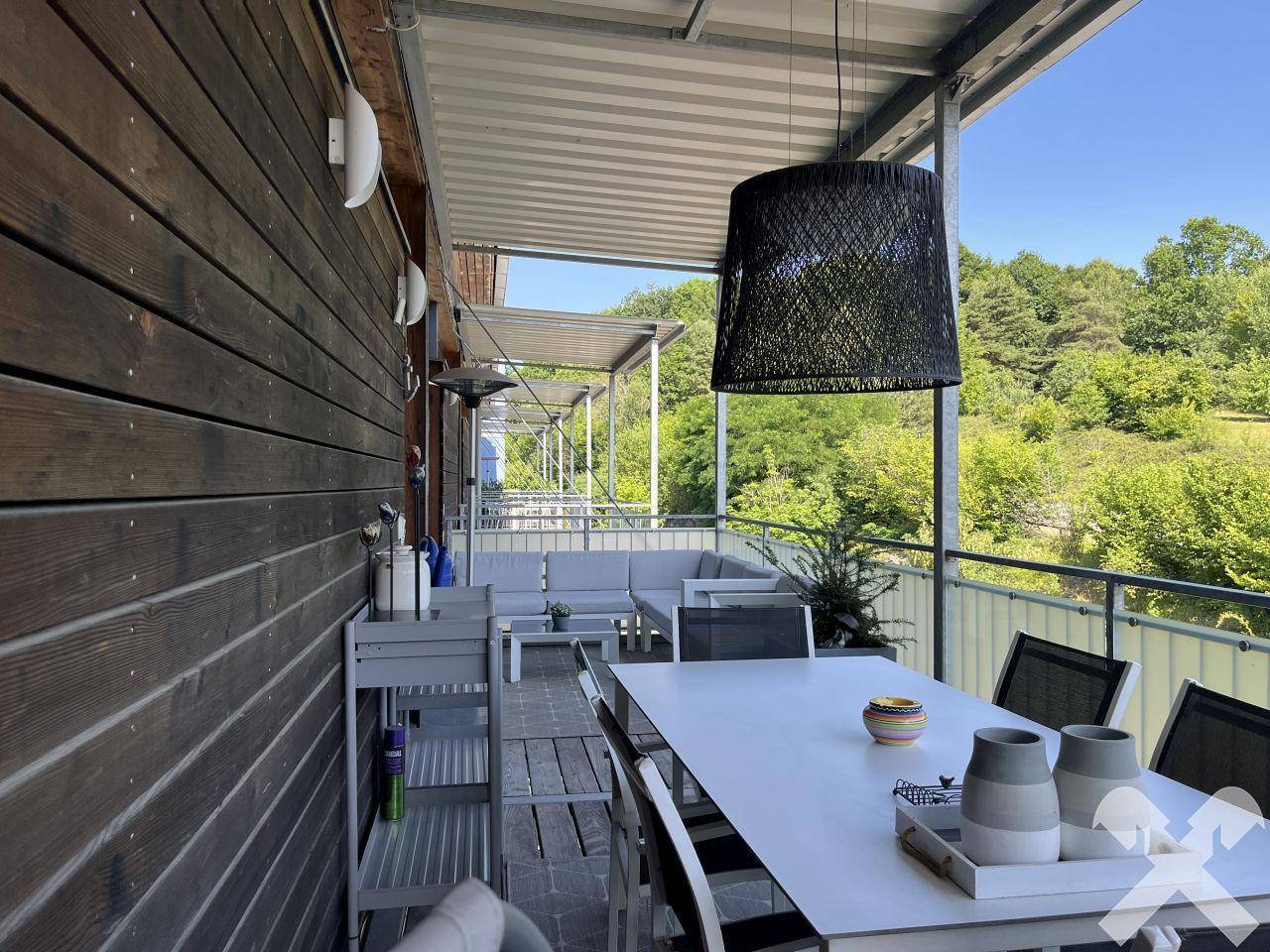 Geräumiger Balkon mit Essbereich und Lounge-Möbeln, umgeben von viel Grün.