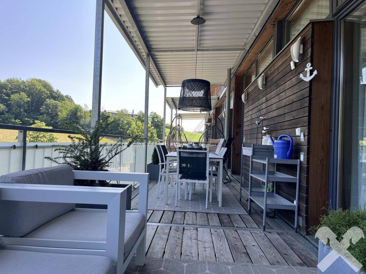 Großer Balkon mit Holzboden, Essbereich und Lounge-Möbeln, ideal zum Entspannen.