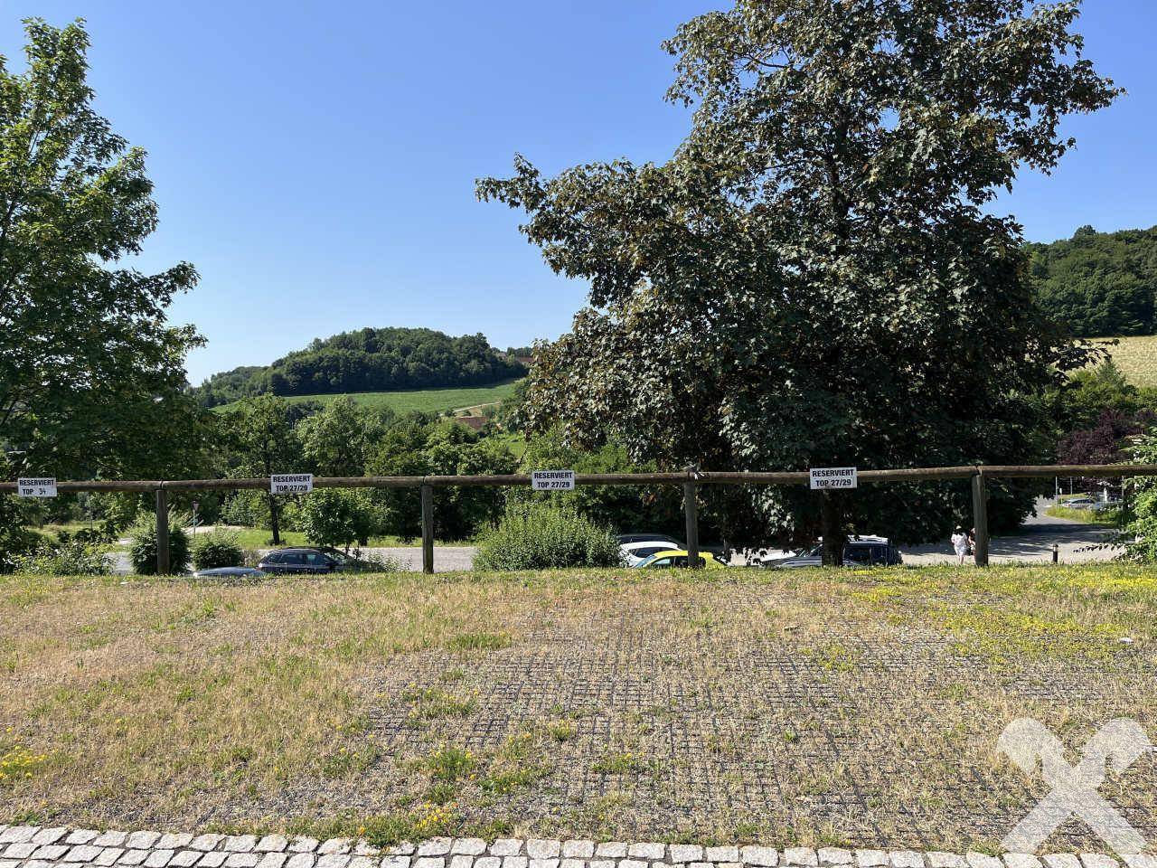 Außenbereich mit Parkplätzen und Blick auf die grüne Hügellandschaft.
