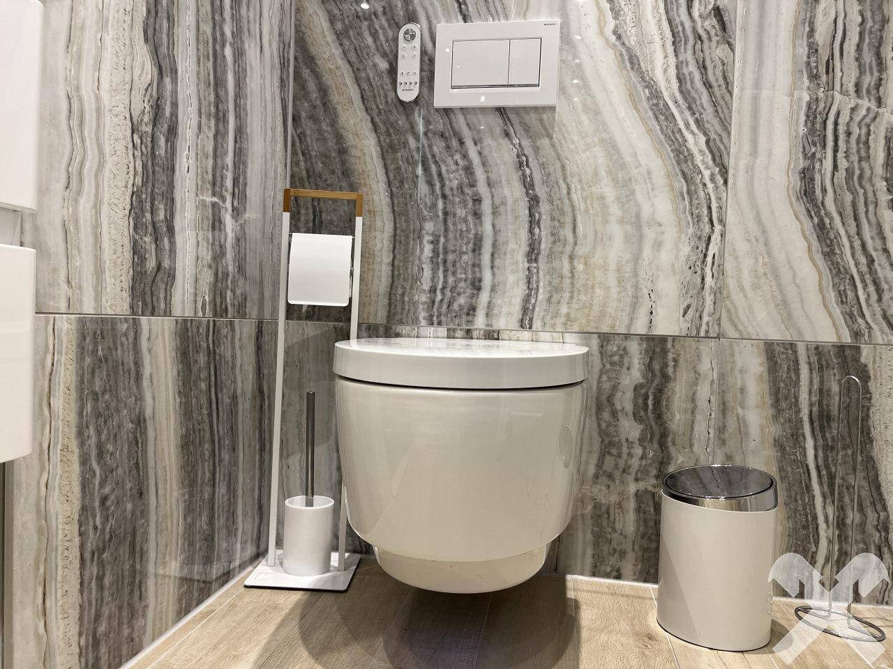 Separate Toilette mit Wand-WC und stilvollen Marmorfliesen an den Wänden.
