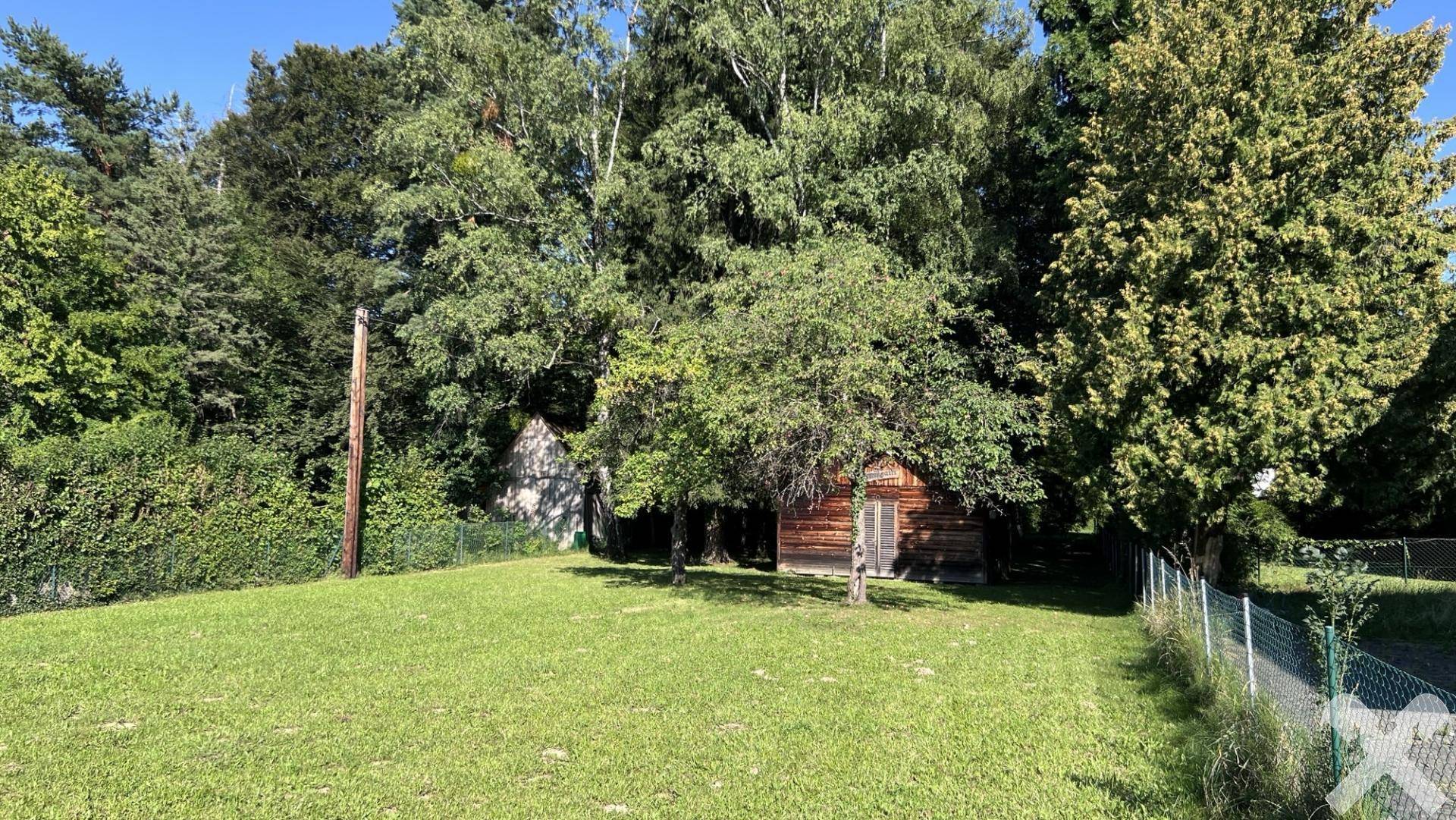 Großzügige Grünfläche mit altem Baumbestand und einem kleinen Holzhaus im hinteren Bereich des Grundstücks.