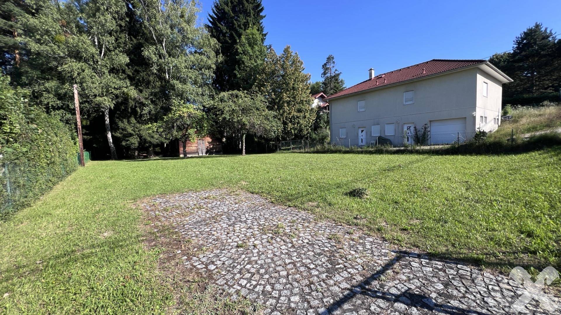 Grüne Grundstücksfläche mit einem gepflasterten Bereich und einem Wohnhaus im Hintergrund.