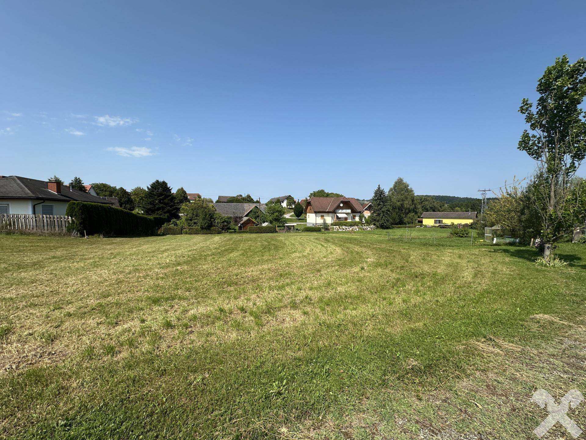 Offenes Feld mit Wohnhäusern und üppiger Vegetation in der Ferne an einem sonnigen Tag.