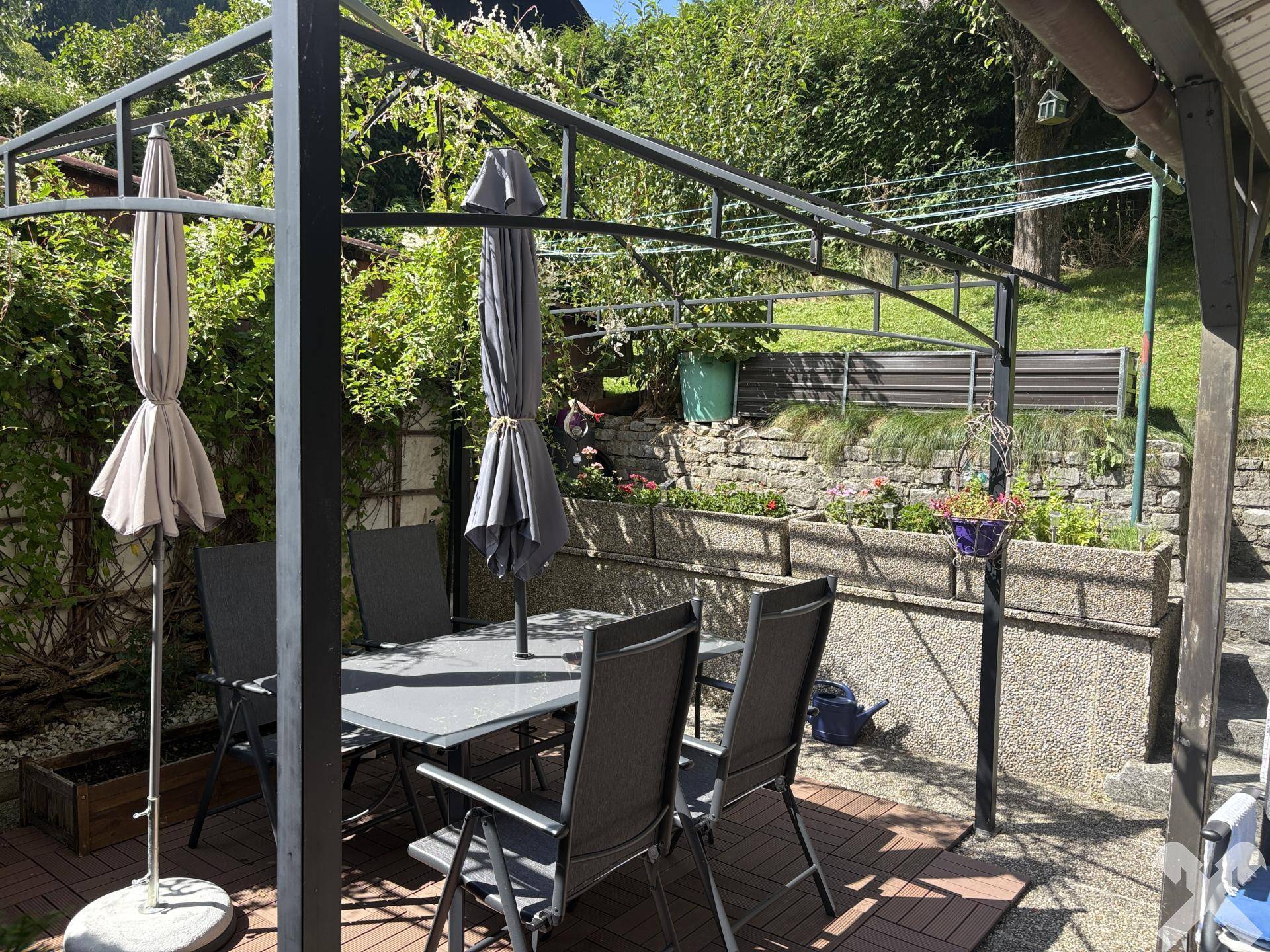 Gemütlicher Sitzbereich im Garten unter einem Pavillon mit Gartenmöbeln und viel Grün.