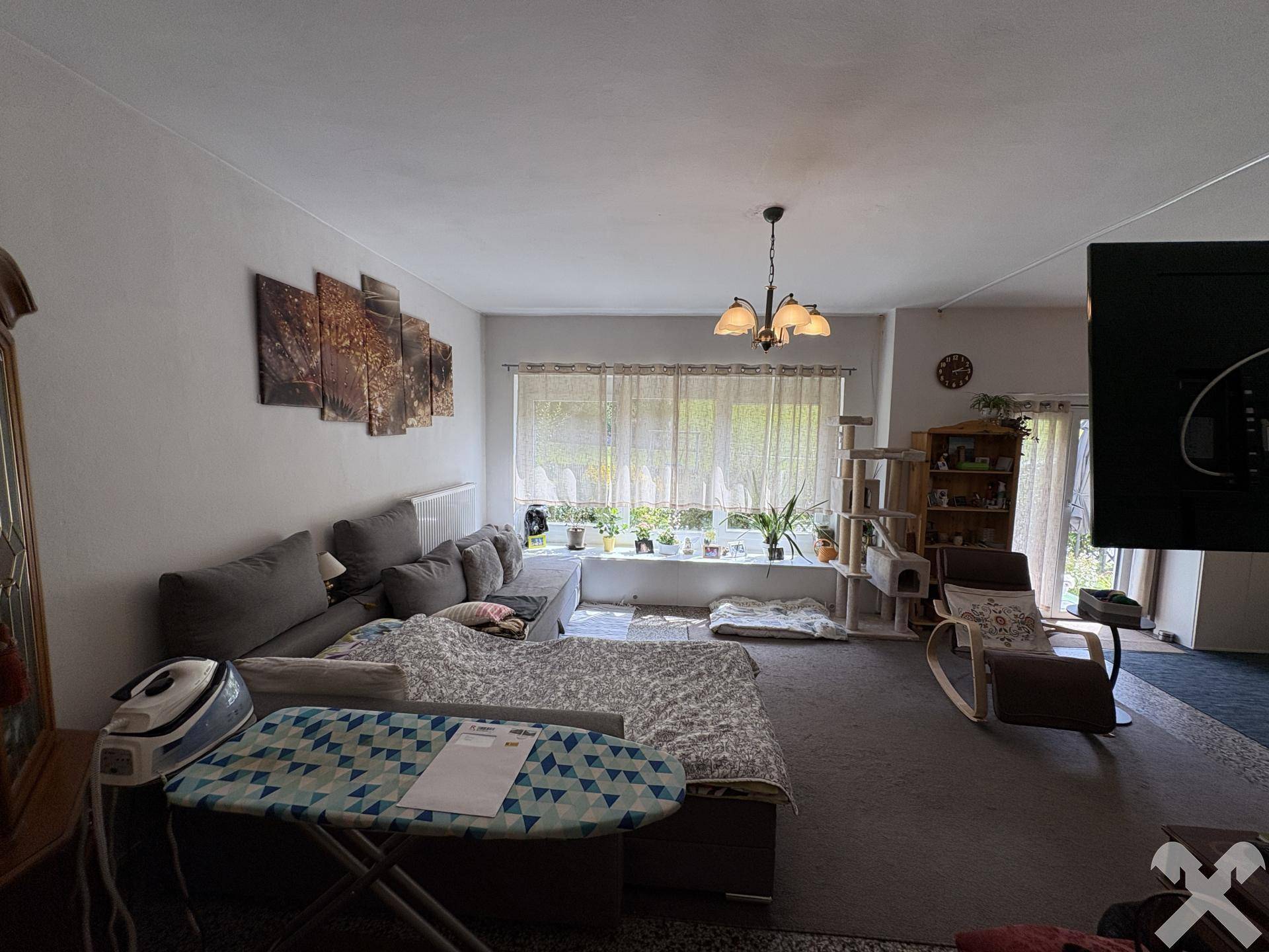 Gemütliches Wohnzimmer mit großem Sofa, Teppichboden und Blick in den Garten.