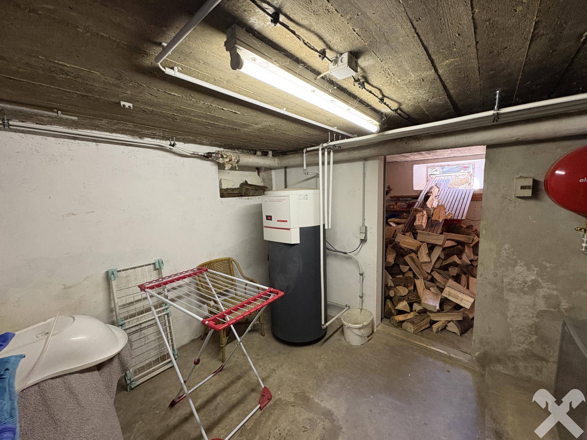 Kellerraum mit Warmwasserspeicher, Wäscheständer und Holzvorrat.