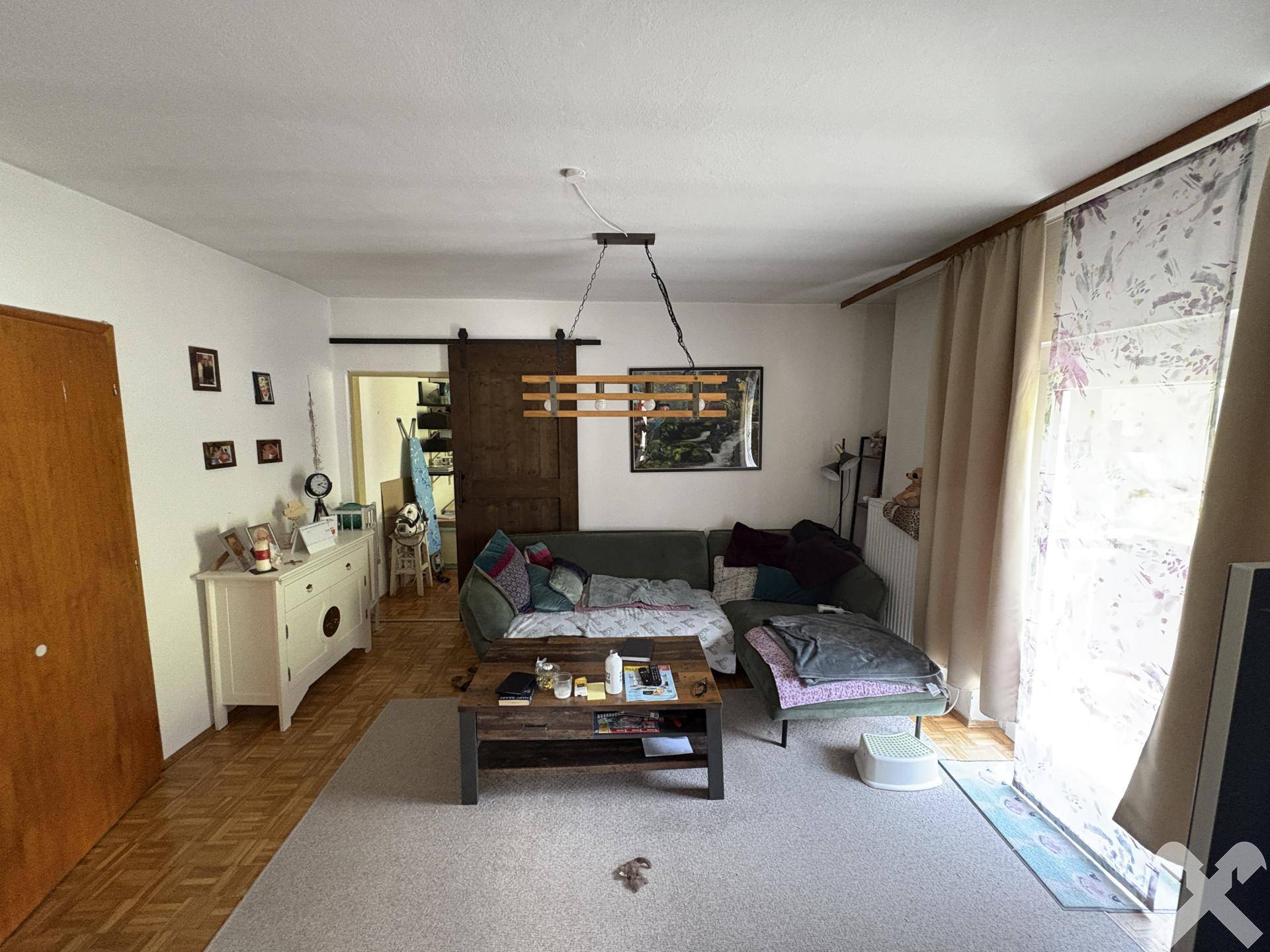 Gemütliches Wohnzimmer mit Sofa, Holzboden und Zugang zu einem weiteren Raum.