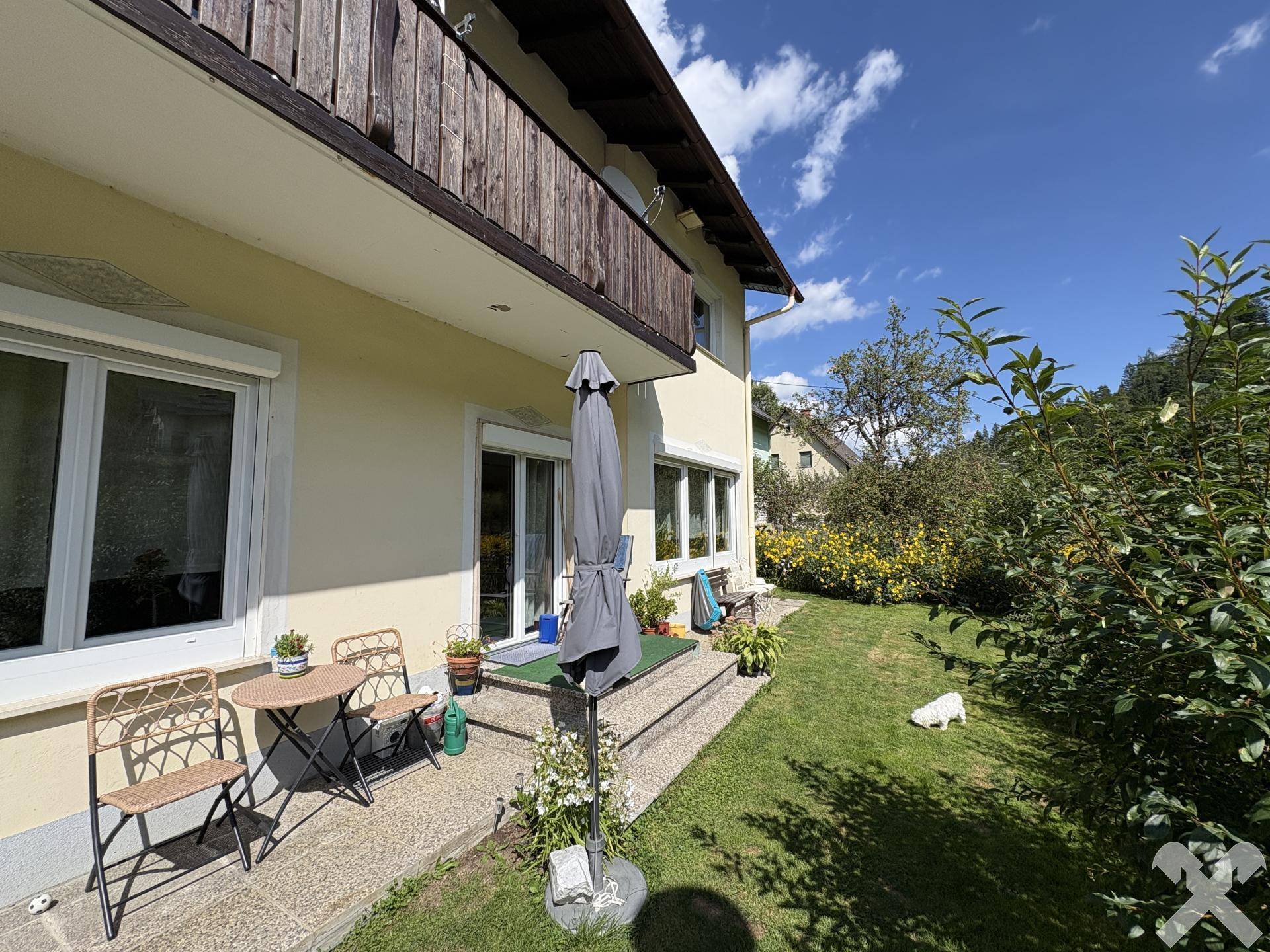 Seitlicher Gartenbereich mit Rasenfläche, kleiner Terrasse und Zugang zum Haus.