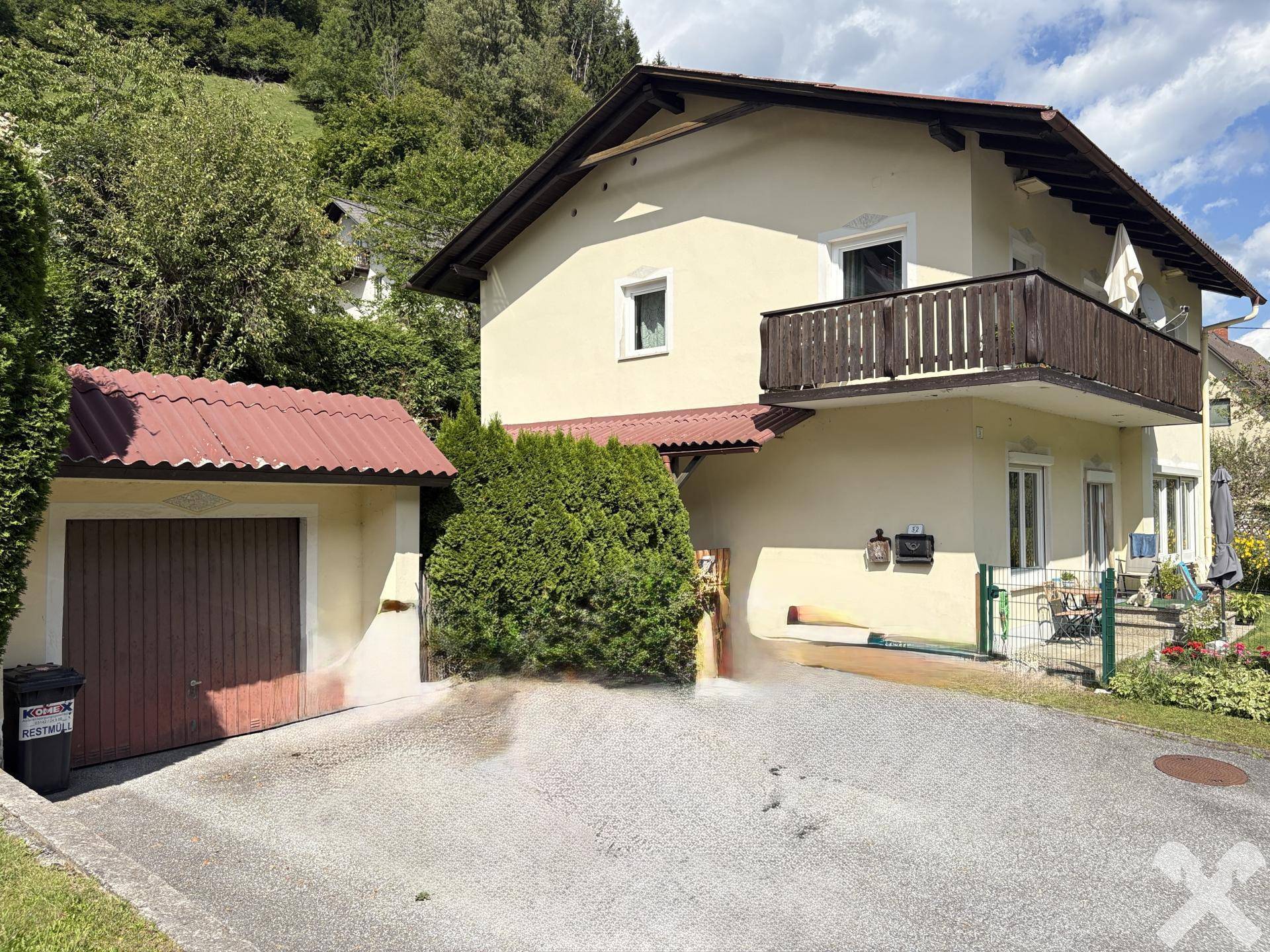 Seitenansicht des Hauses mit Garage, Zufahrt und Blick auf die umliegende grüne Landschaft.