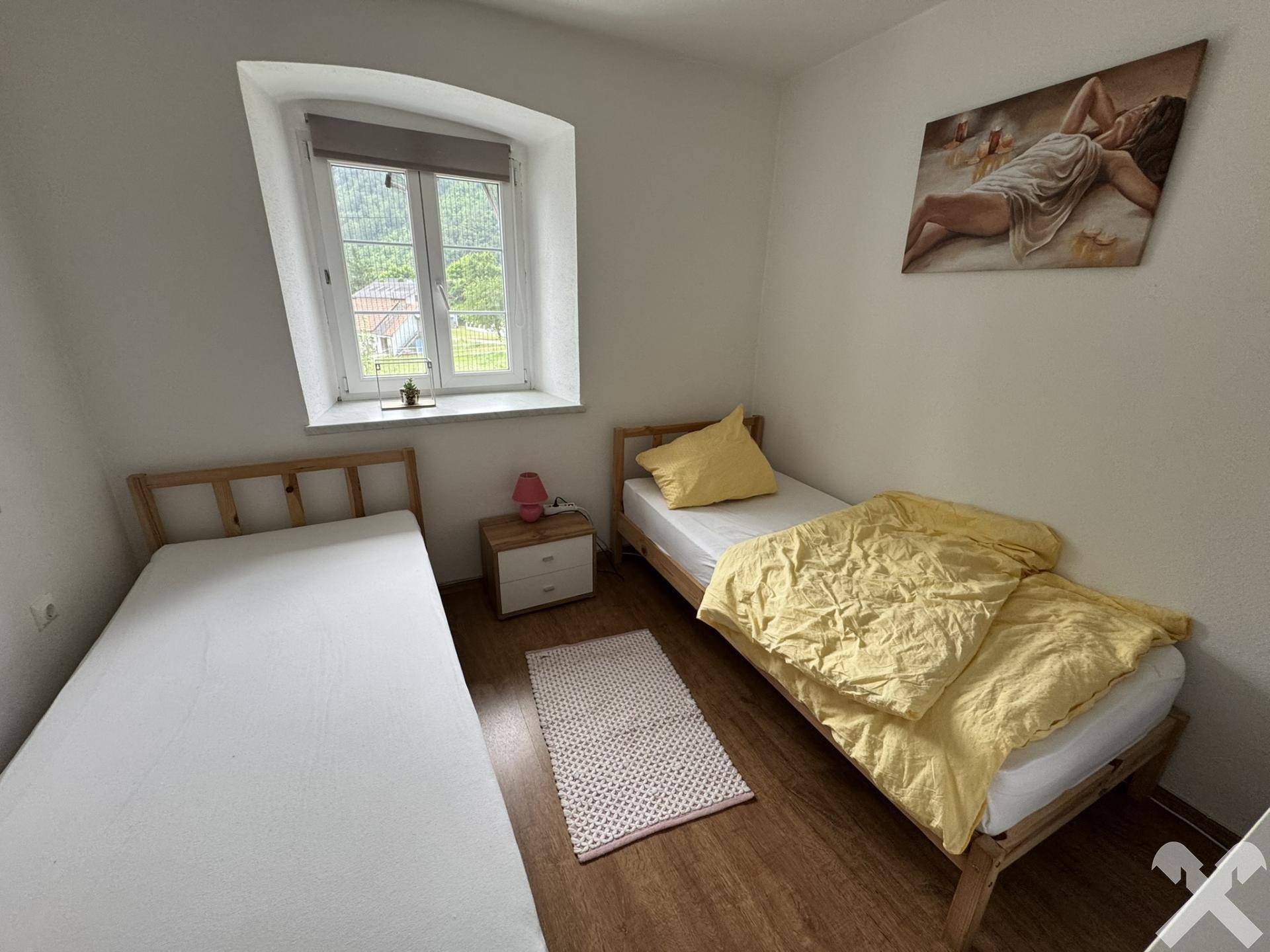 Schlafzimmer mit zwei Einzelbetten, Holzboden und Blick ins Grüne.