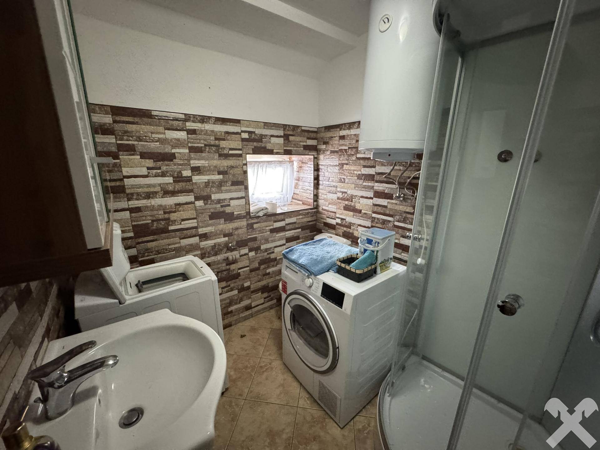 Badezimmer mit Duschkabine, Waschmaschine und gefliesten Wänden.