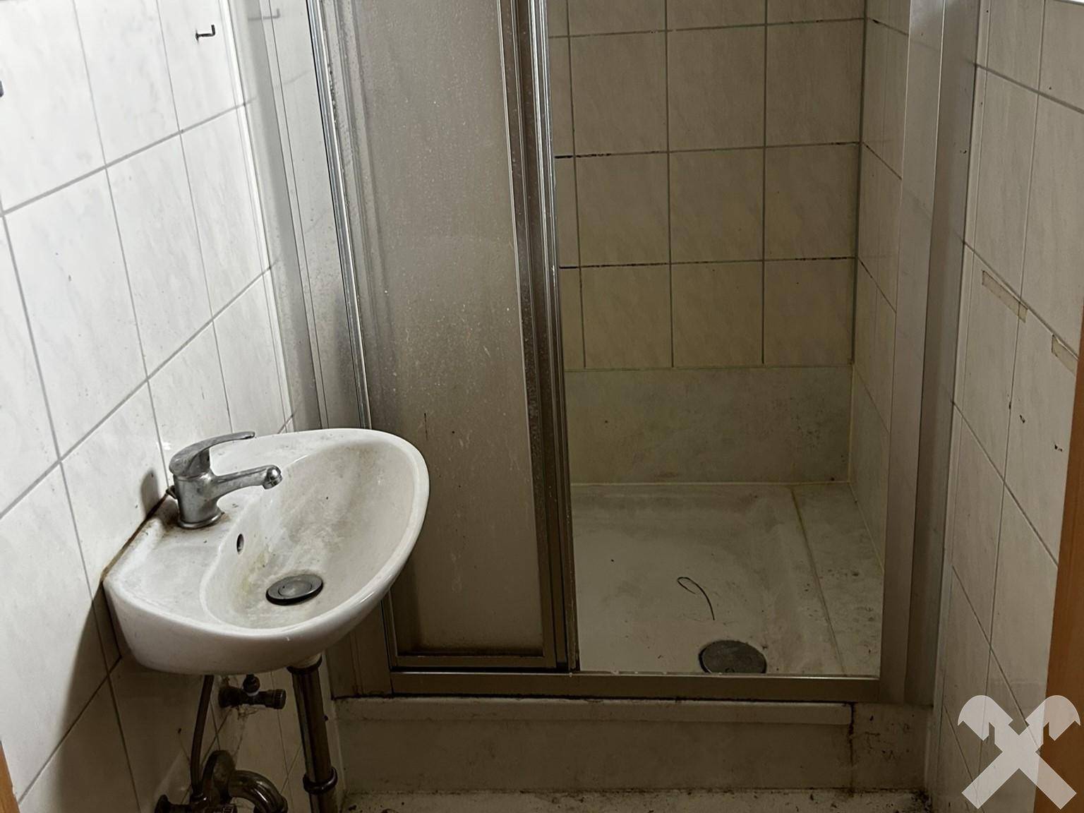 Einfaches Badezimmer mit Duschkabine und Waschbecken, das eine Renovierung benötigt.