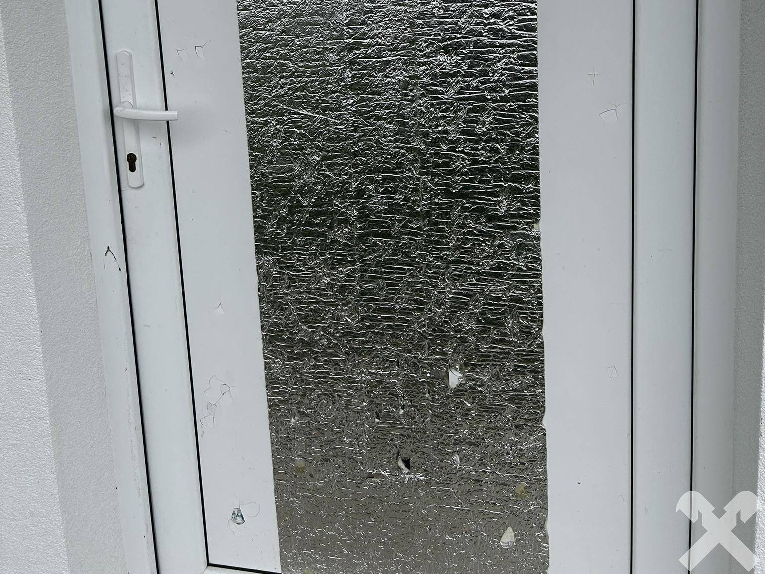 Nahaufnahme einer weißen Tür mit einer reflektierenden Folie, die Renovierungsbedarf zeigt.