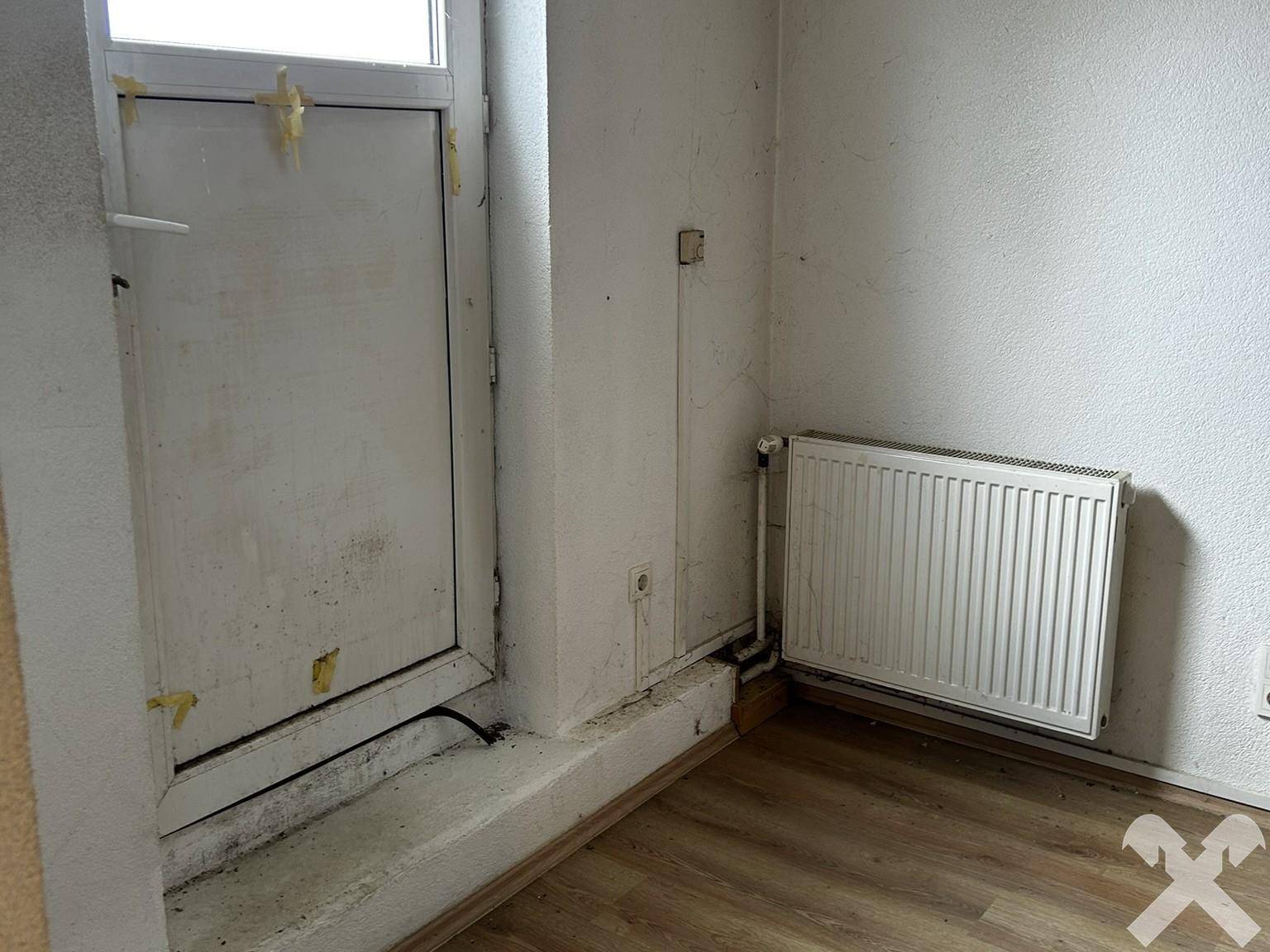 Raum mit Tür, Heizkörper und sichtbaren Gebrauchsspuren, der eine Renovierung erfordert.