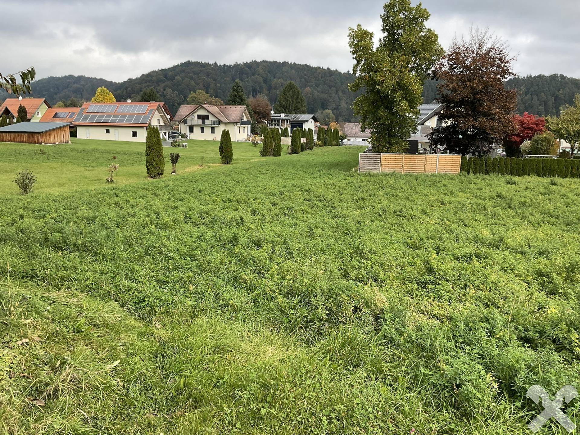 Weitläufiges grünes Grundstück mit Blick auf umliegende Wohnhäuser und bewaldete Hügel.