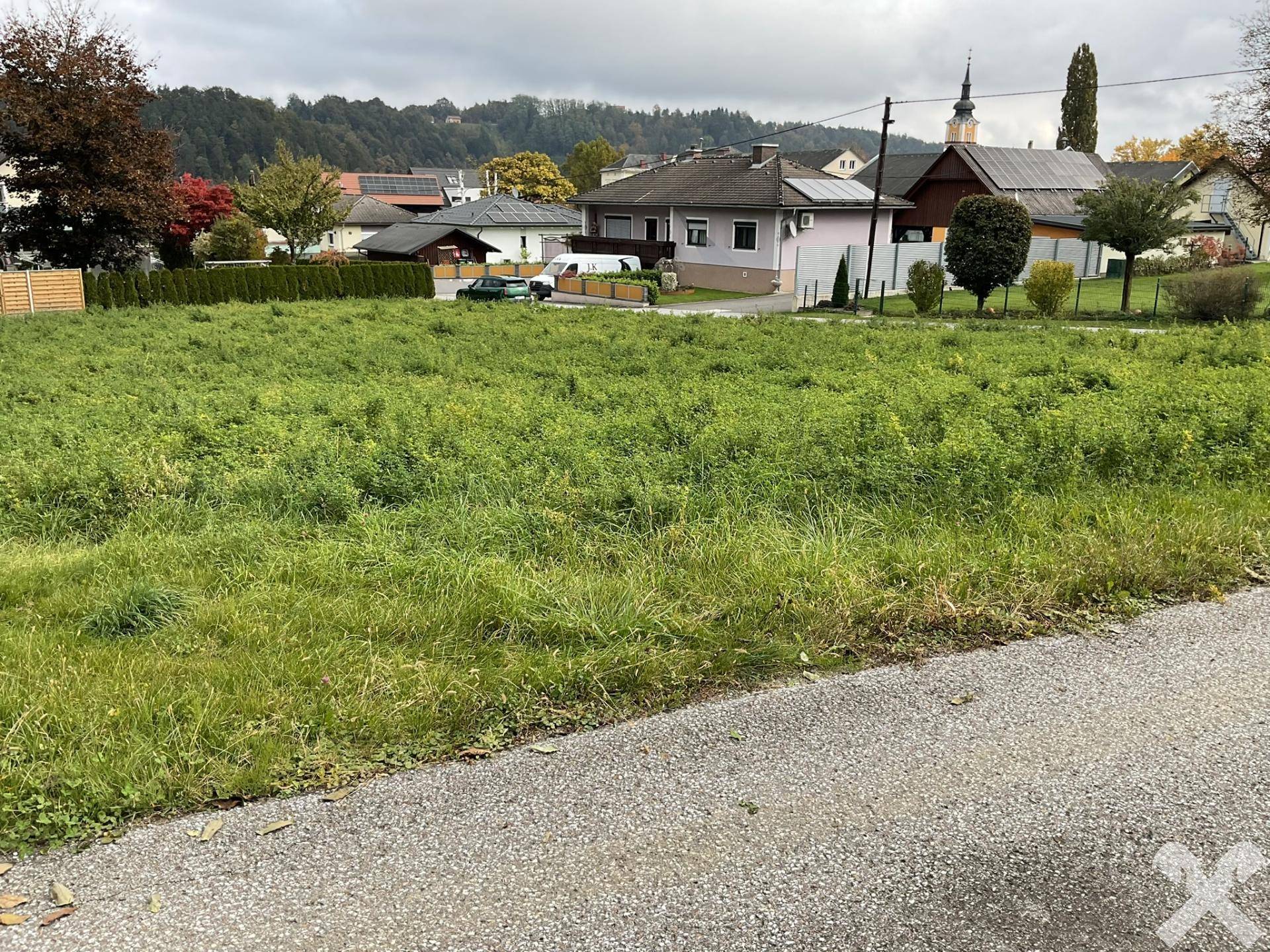 Grünes Baugrundstück mit Blick auf die Nachbarschaft und einen Kirchturm in der Ferne.