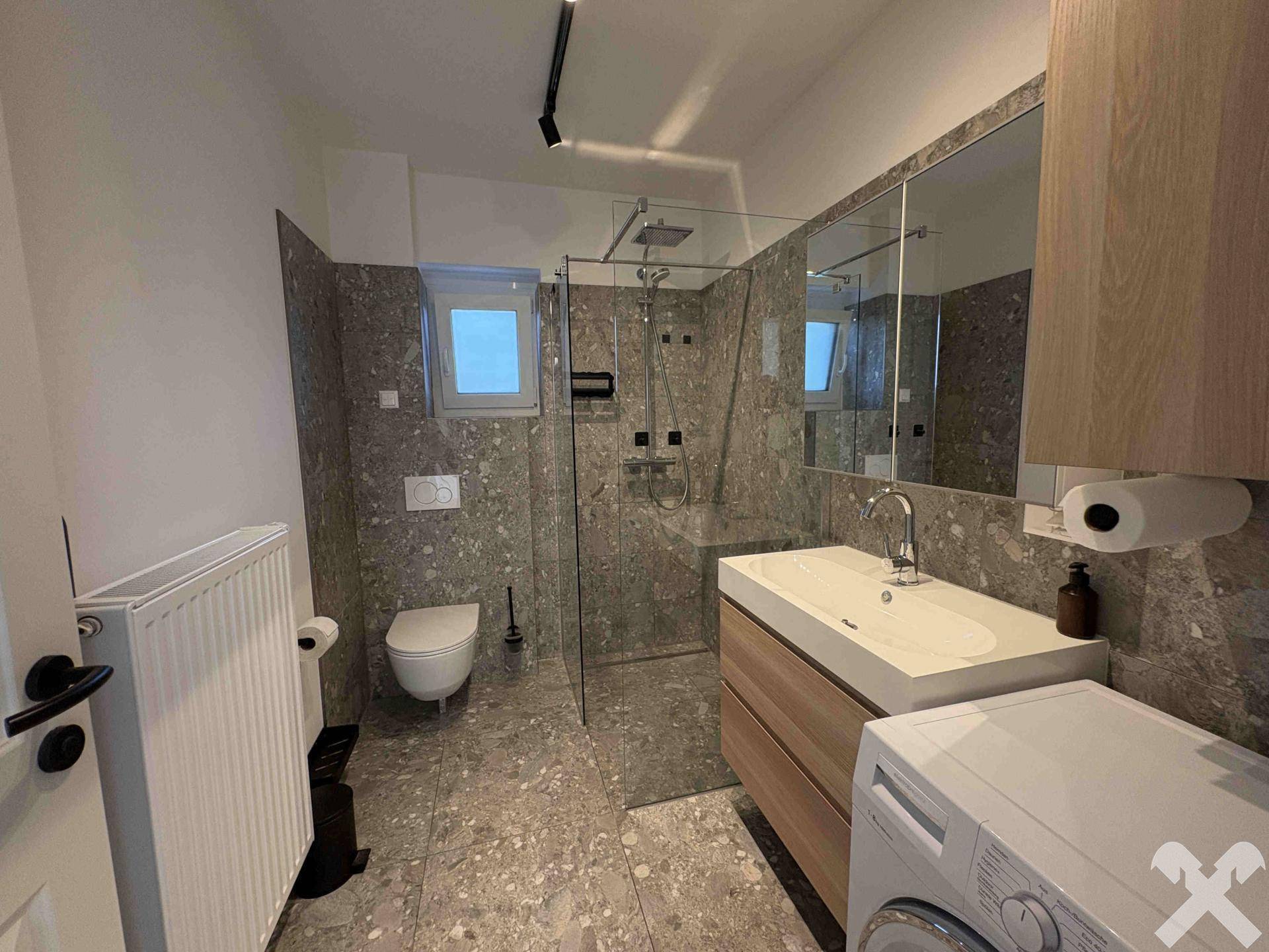 Modernes Badezimmer mit großer begehbarer Dusche, Waschtisch und Waschmaschine.