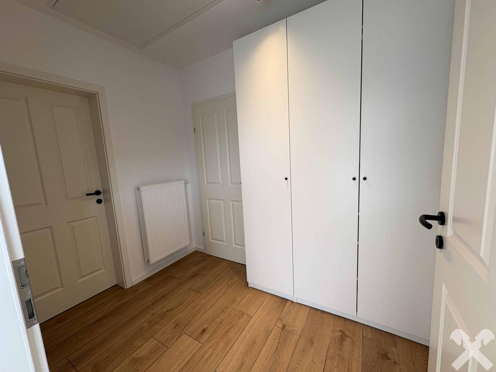Kleiner Raum mit weißem Kleiderschrank, Heizkörper und Holzboden.