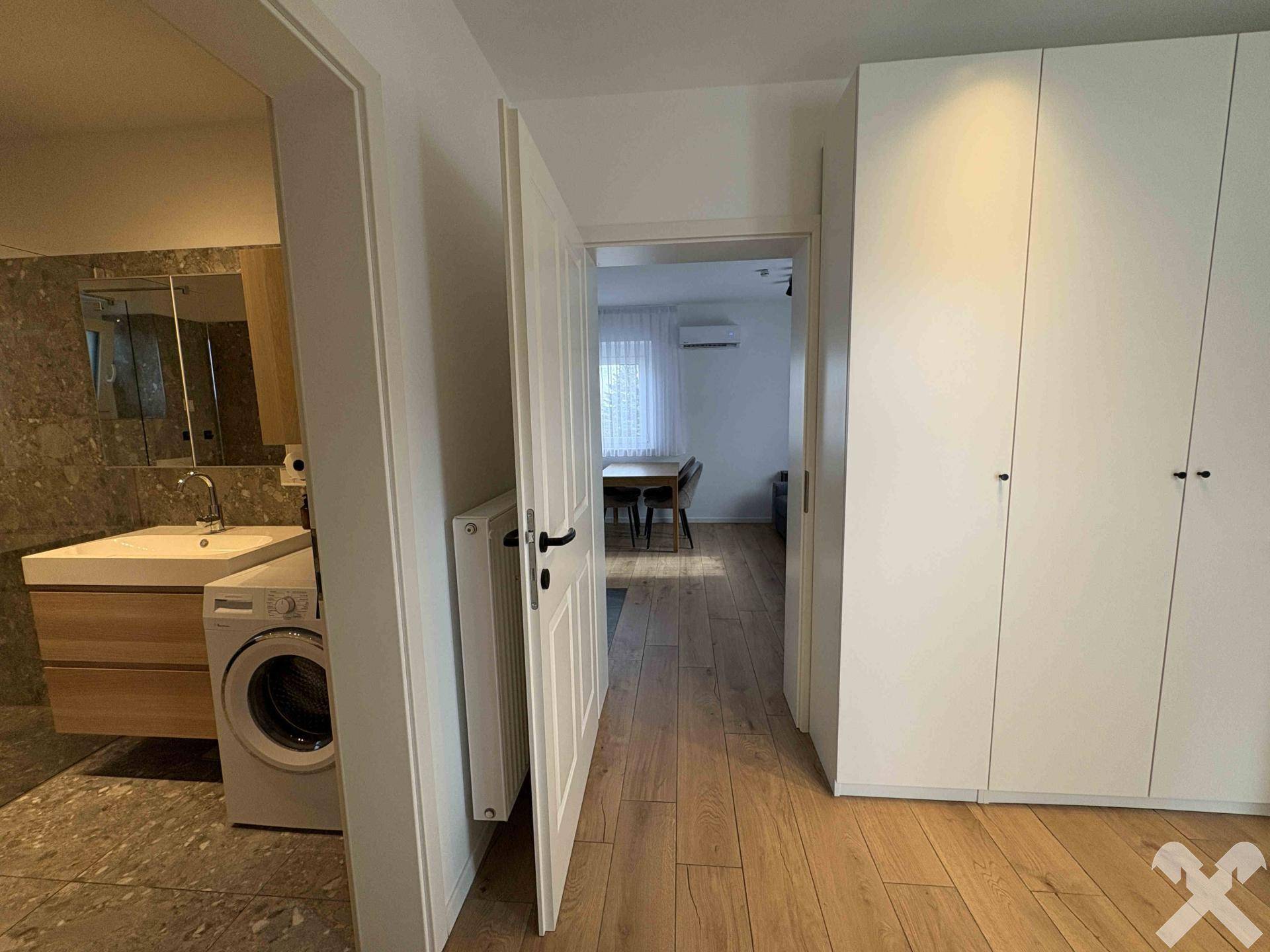 Übergangsbereich mit Holzboden, weißem Kleiderschrank und Blick ins Badezimmer.