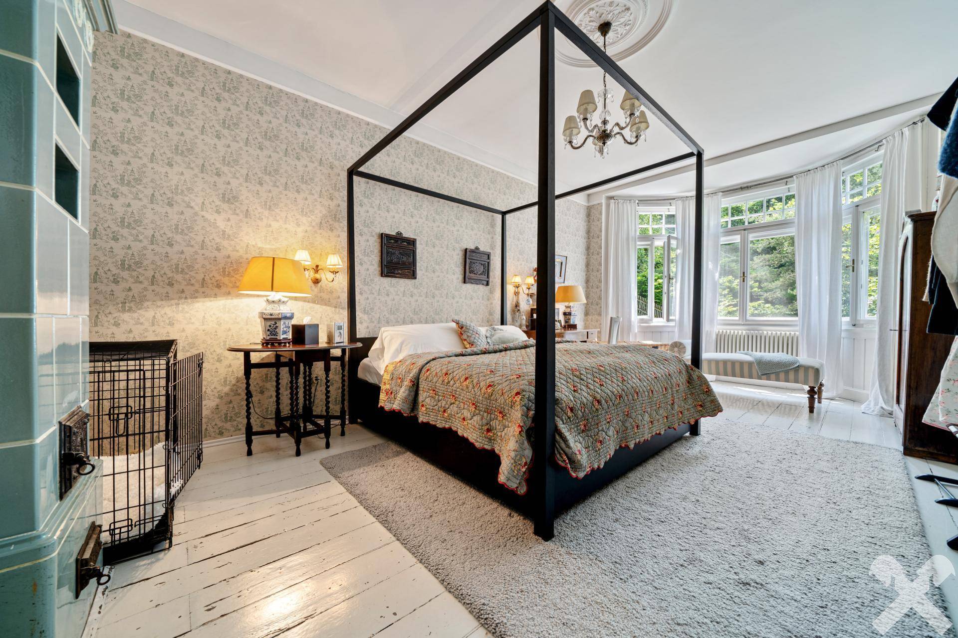 Elegantes Schlafzimmer mit Himmelbett, Kachelofen und großen Fenstern mit viel Licht.