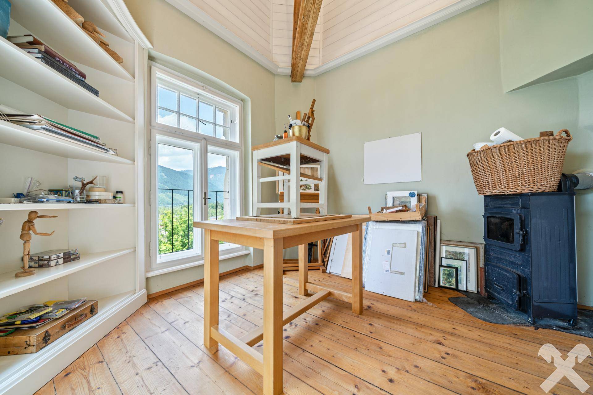 Helles Atelier im Dachgeschoss mit Holzboden, sichtbaren Balken und Bergblick.