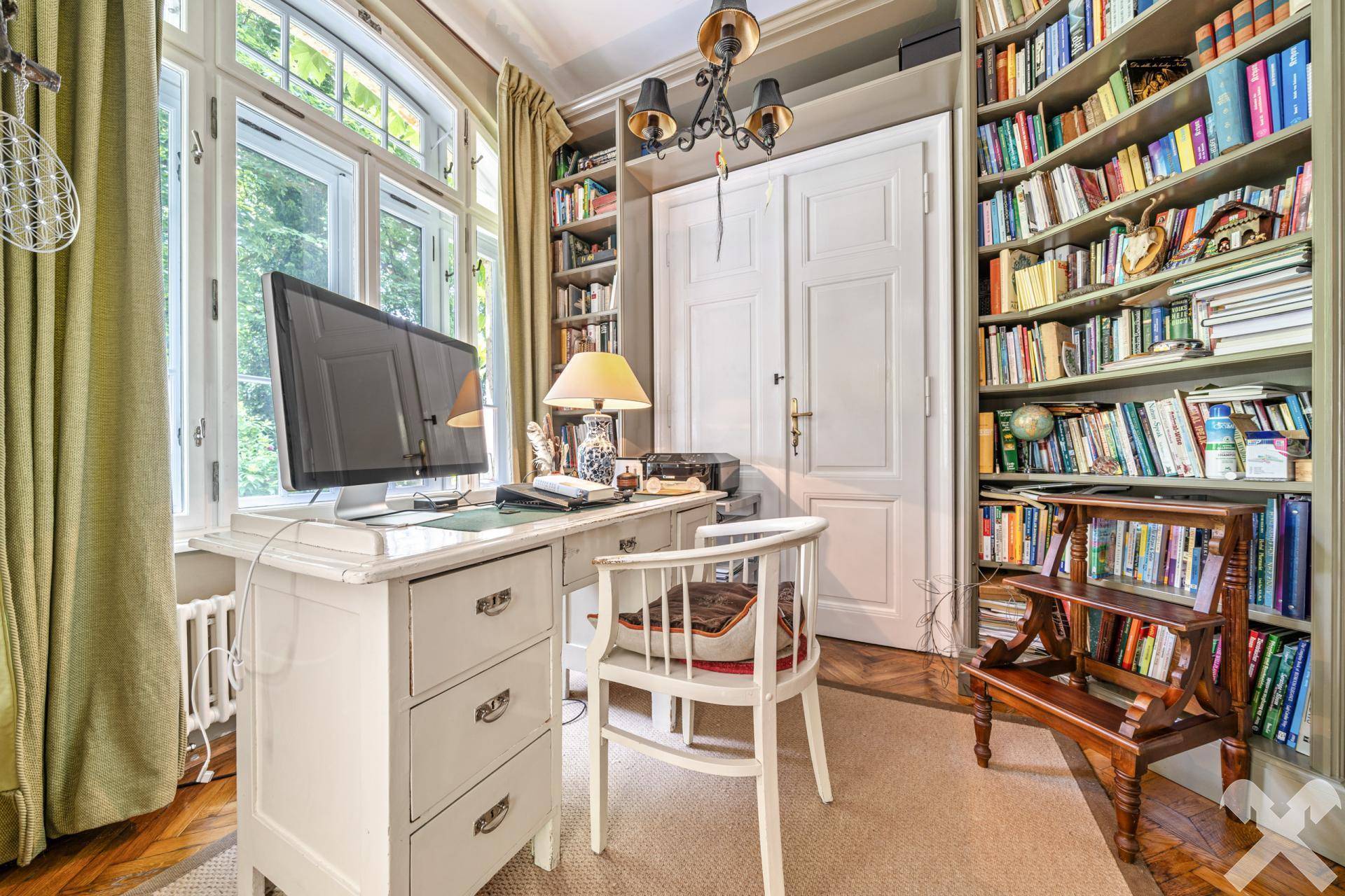 Helles Arbeitszimmer mit Schreibtisch, Bücherregalen und Blick in den Garten.