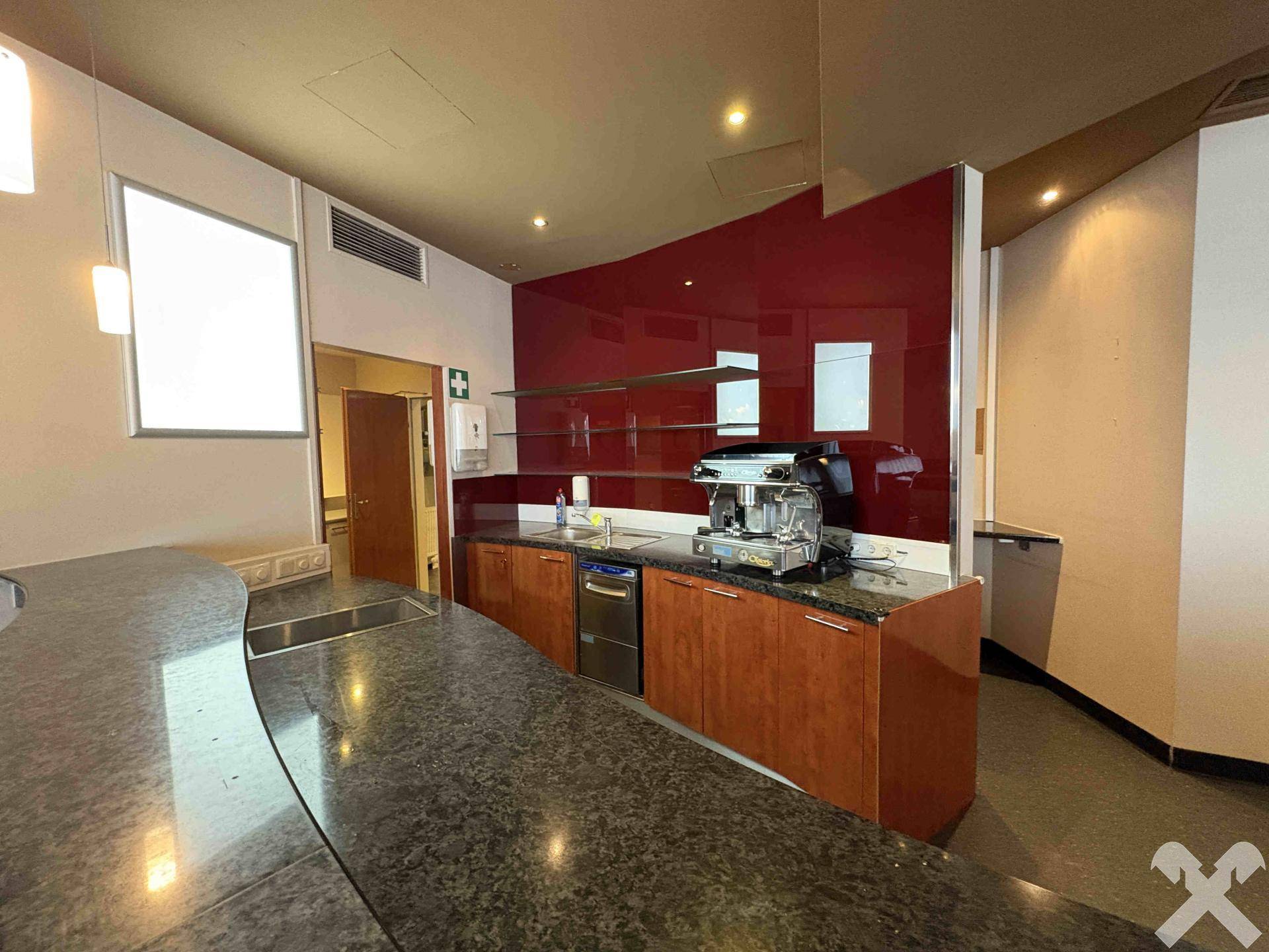 Detailansicht der Küchenzeile mit Spülbecken, Kaffeemaschine und roter Glasrückwand.