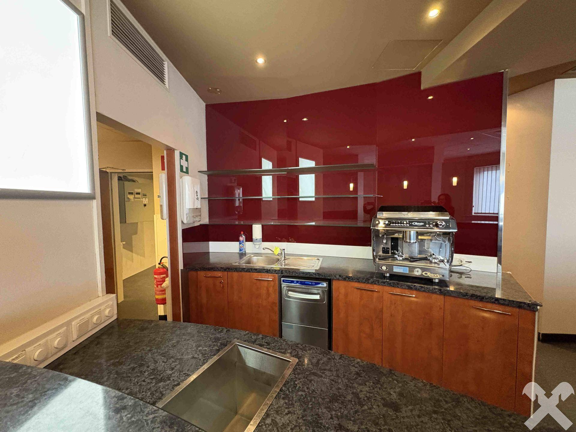 Küchenzeile mit roter Glasrückwand, Spülbecken, Geschirrspüler und professioneller Kaffeemaschine.