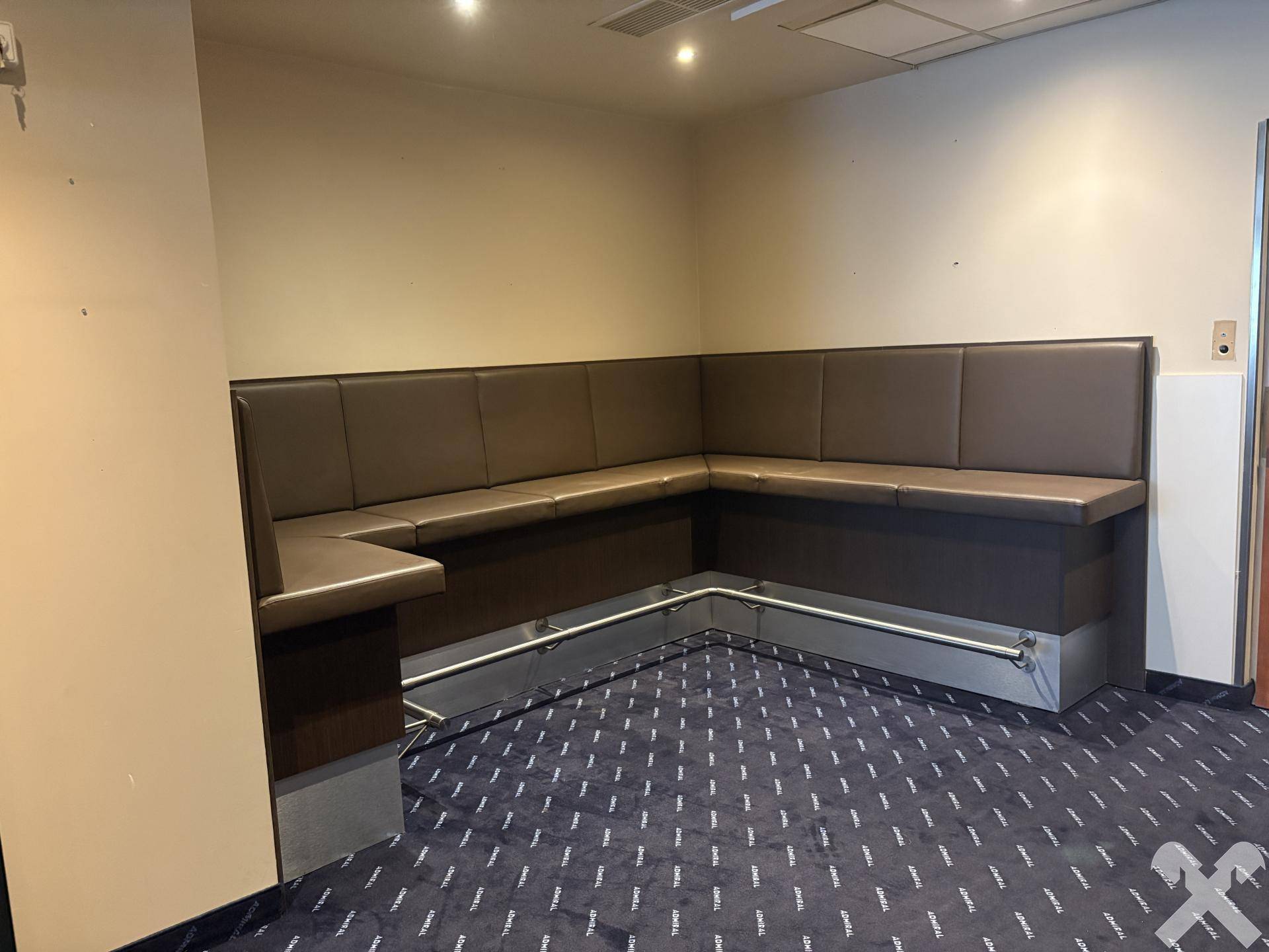 Braune Eckbank mit Polstern und Metallfußstütze in einem Raum mit Teppichboden.