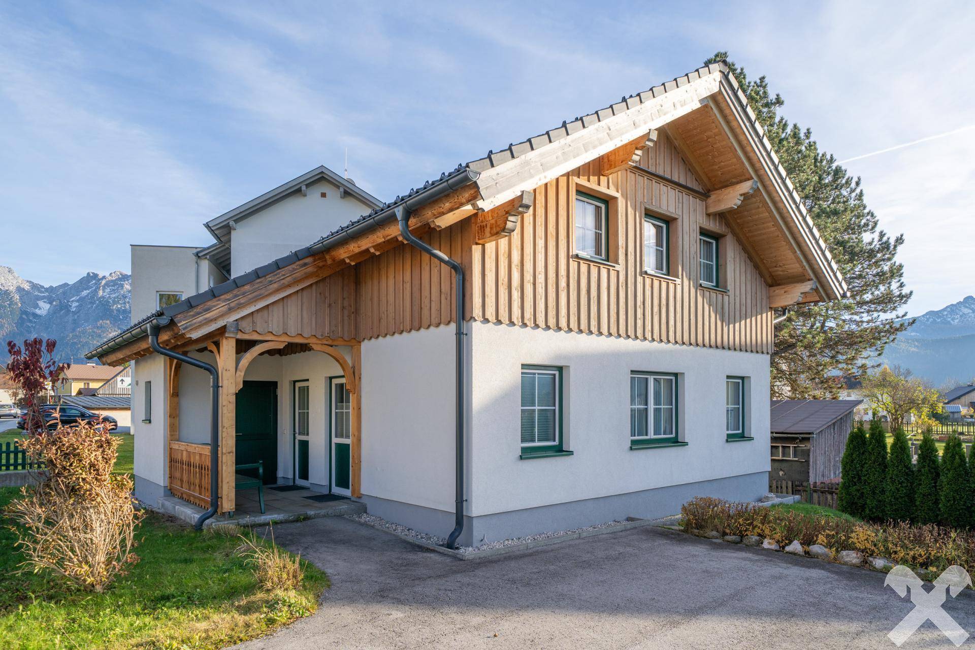 Charmantes Haus mit Holzbalkonen und Satteldach, umgeben von grüner Landschaft und Bergen.