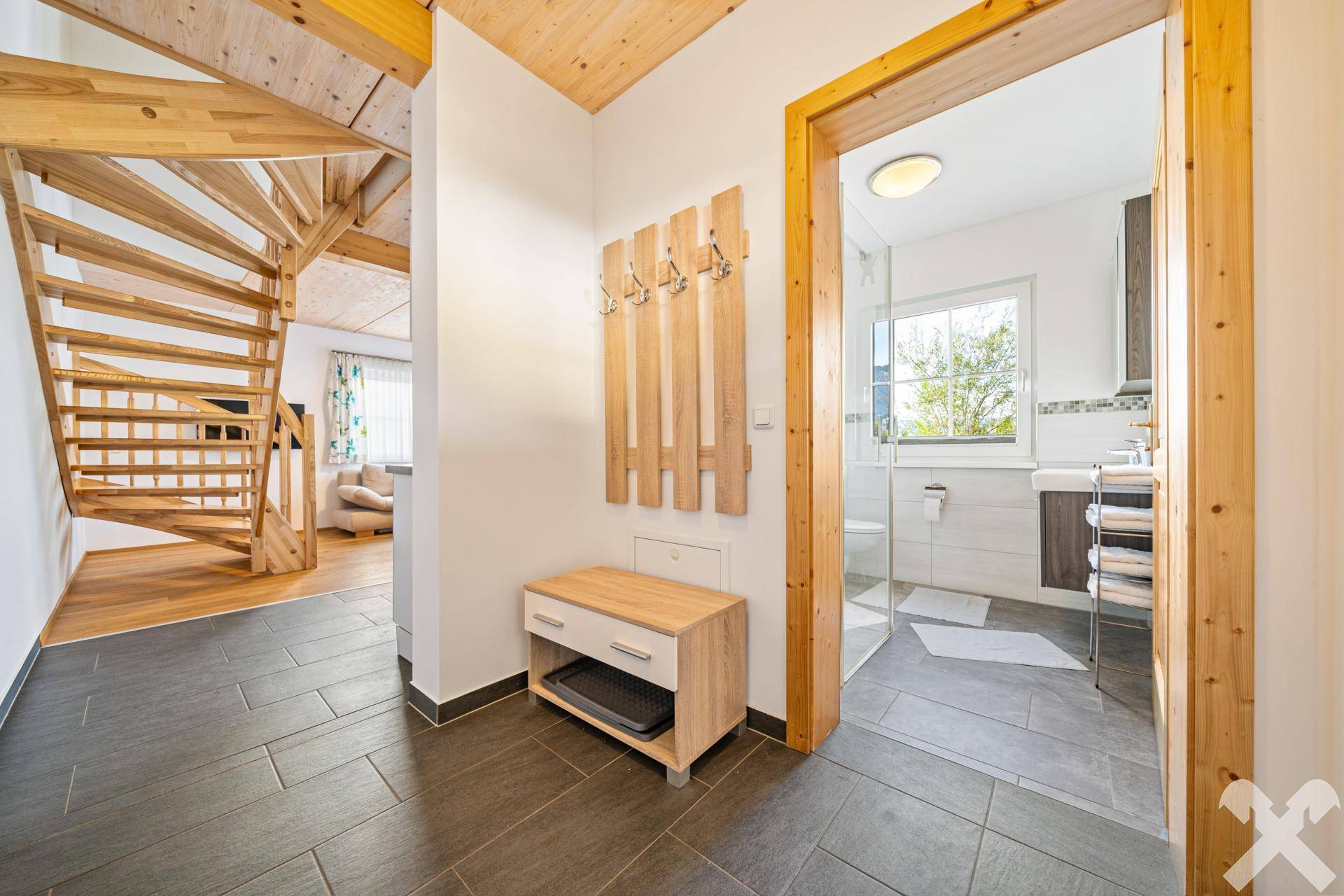Heller Flur mit Holztreppe und Zugang zu einem modernen Badezimmer, ausgestattet mit Fliesenboden.