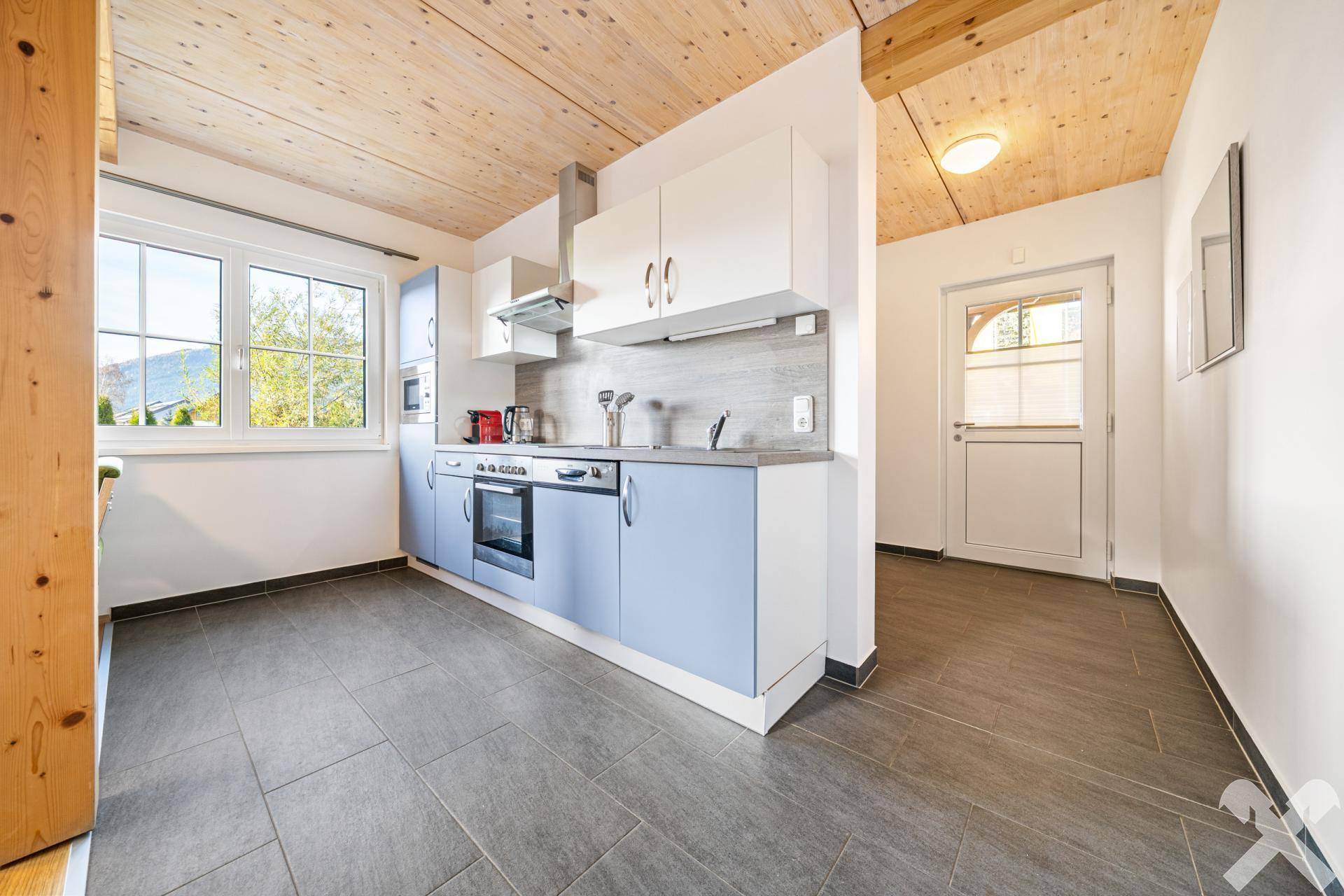 Moderne Einbauküche mit hellblauen und weißen Fronten, Fliesenboden und viel Tageslicht.