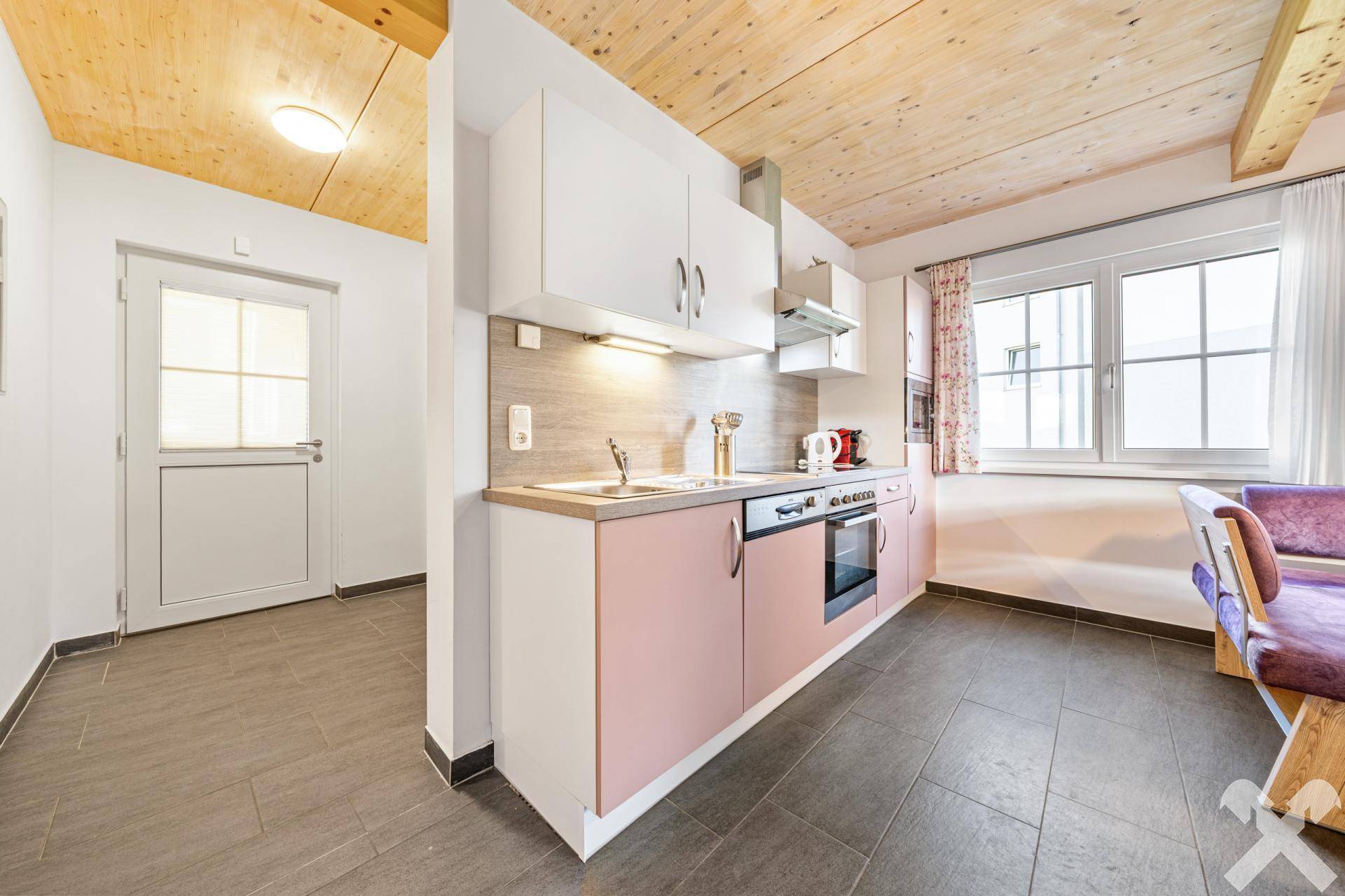 Moderne Einbauküche mit rosa und weißen Fronten, Fliesenboden und viel Tageslicht.