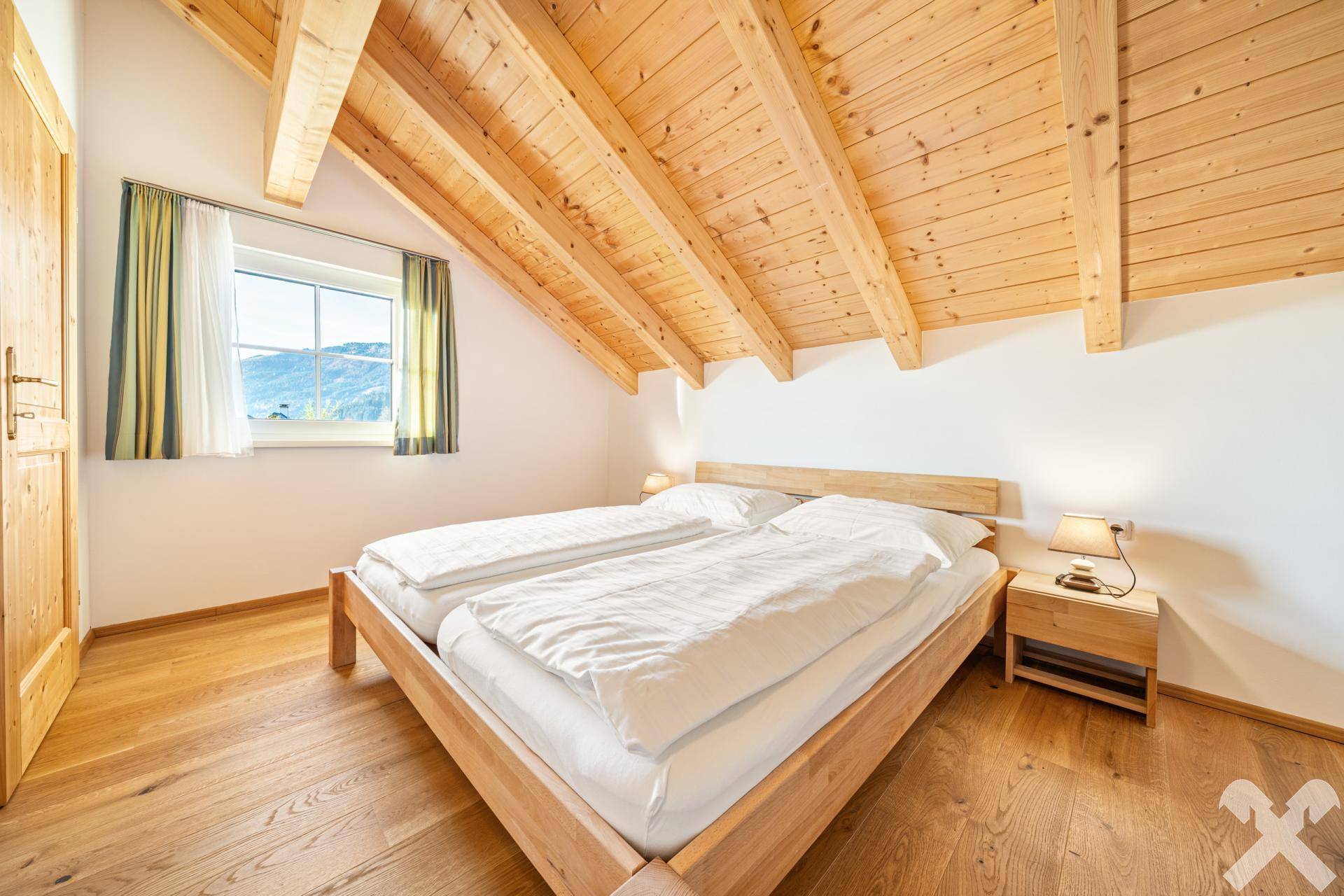 Geräumiges Schlafzimmer im Dachgeschoss mit Holzbalken, Holzboden und Fenster mit Bergblick.