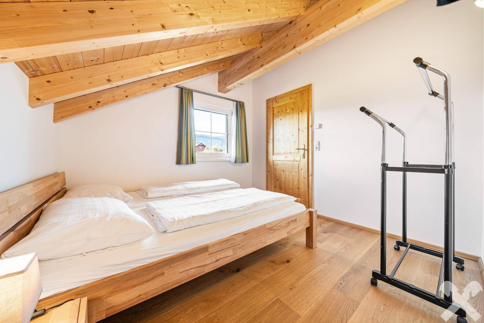 Helles Schlafzimmer im Dachgeschoss mit Holzbalkendecke, Holzboden und Bergblick.