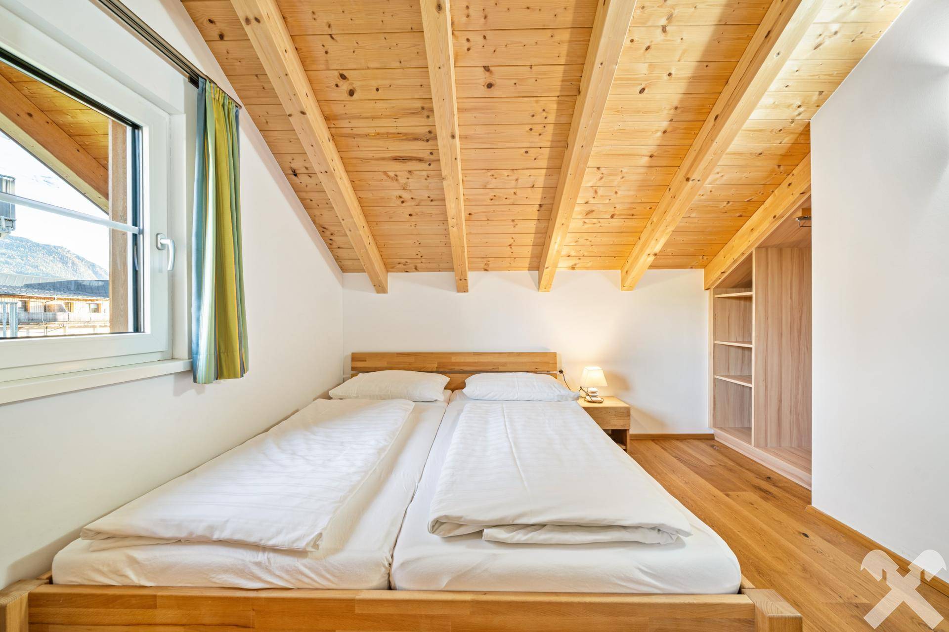 Helles Schlafzimmer im Dachgeschoss mit Holzbalkendecke, Holzboden und Einbauschrank.