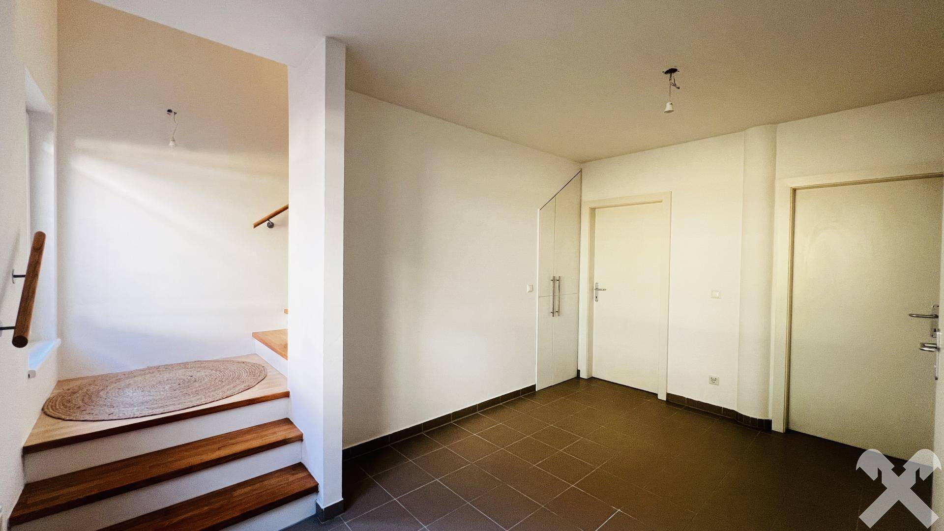 Heller Eingangsbereich mit Fliesenboden, Holztreppe und Zugang zu weiteren Räumen.