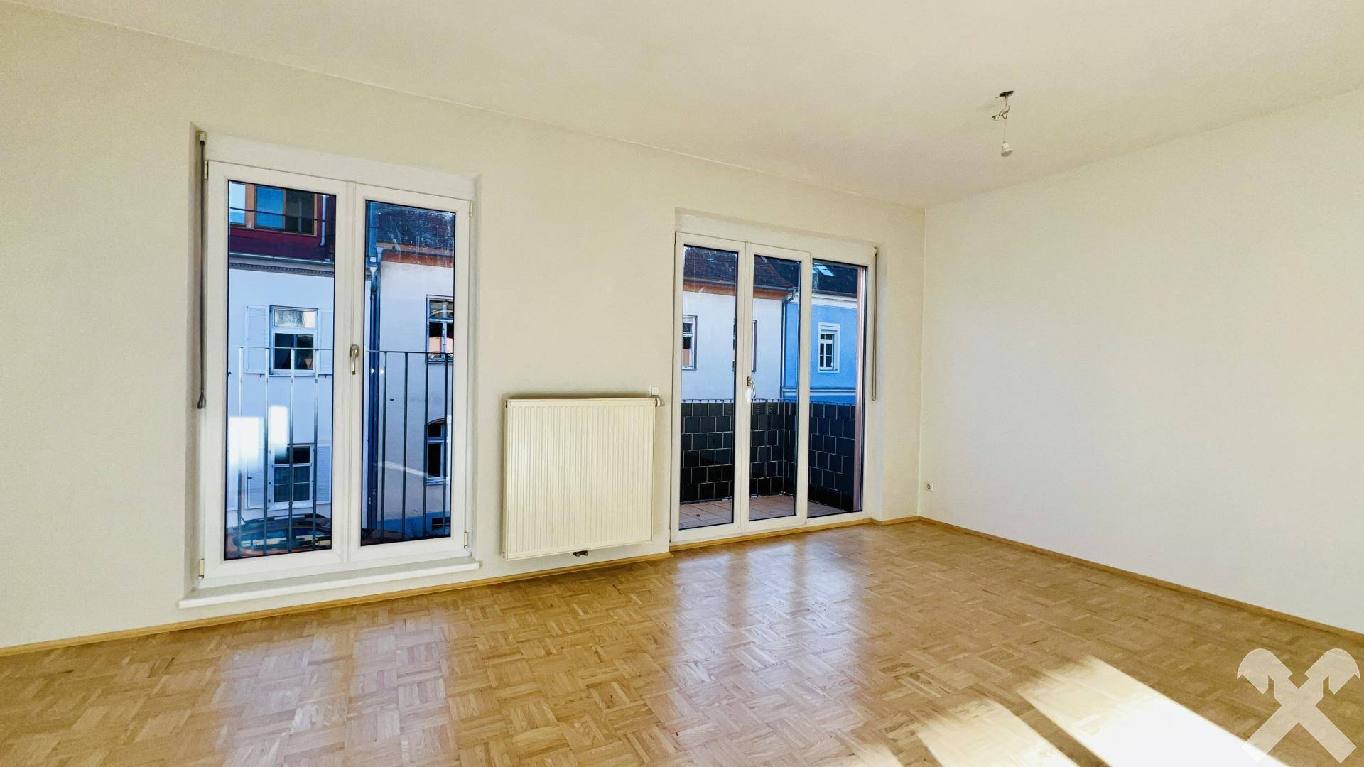 Helles, leeres Zimmer mit Parkettboden und Zugang zu zwei französischen Balkonen.