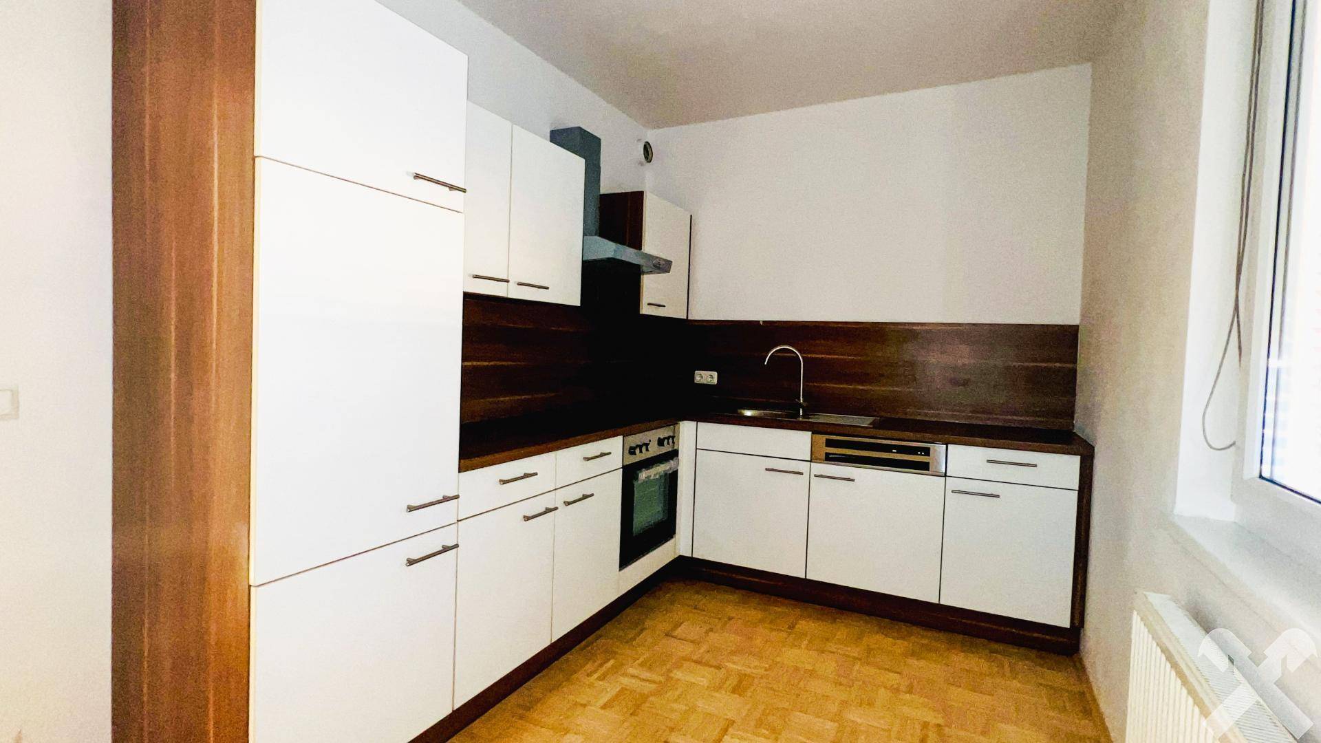 Moderne Einbauküche mit weißen Schränken, Holzdetails und Parkettboden.