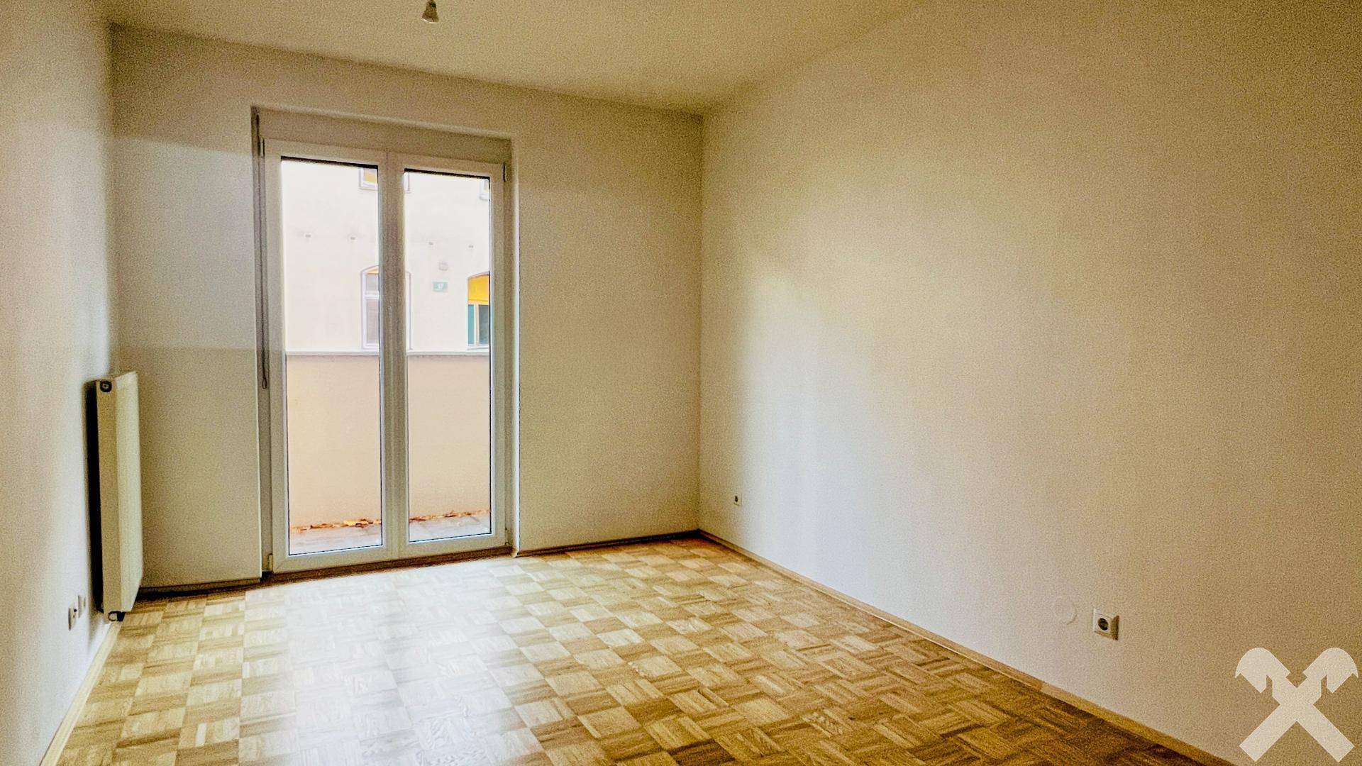 Helles Schlafzimmer mit Parkettboden und Zugang zu einem französischen Balkon.