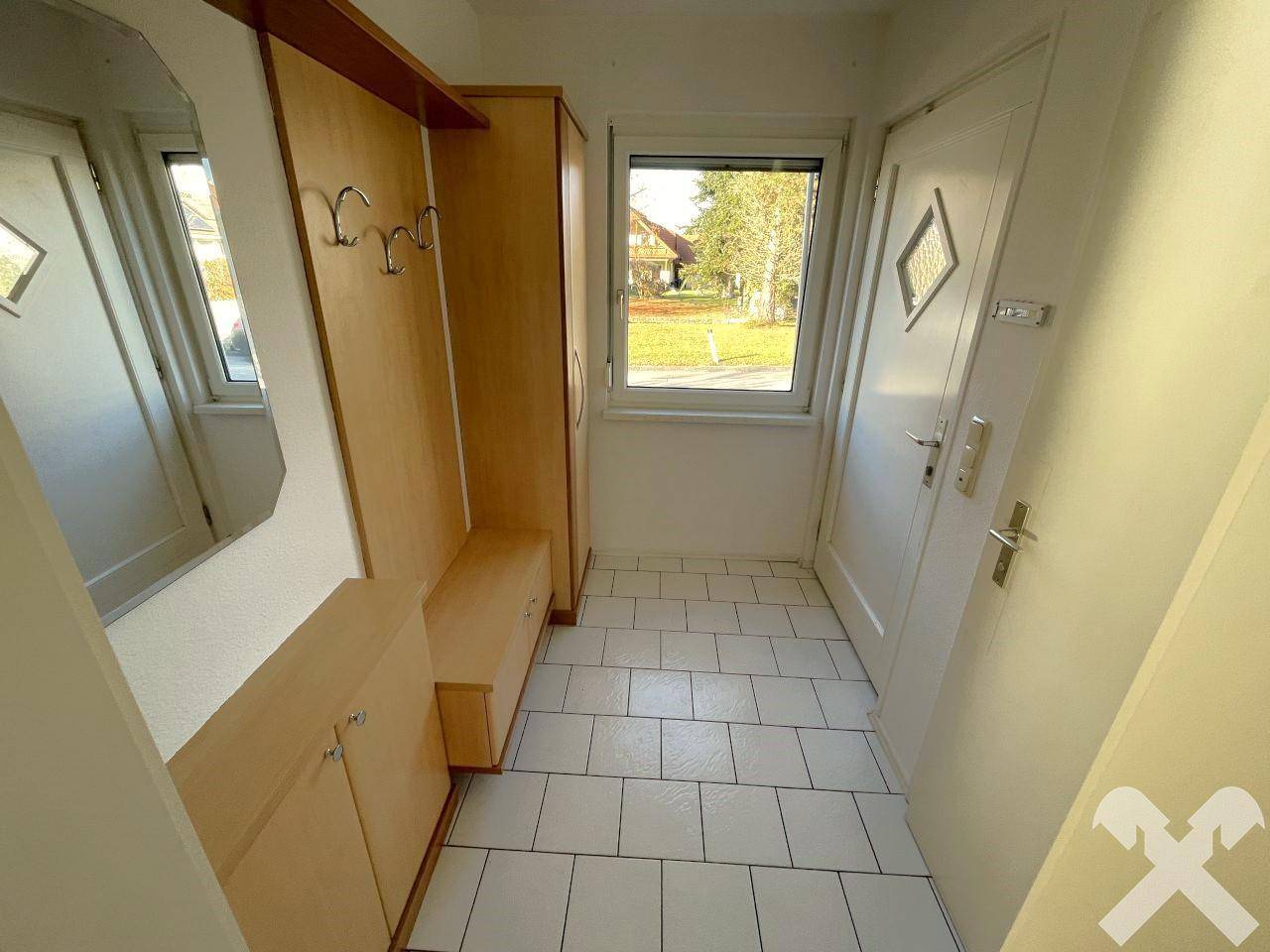 Heller Eingangsbereich mit Fliesenboden, Garderobe und Fenster zur Straßenseite.