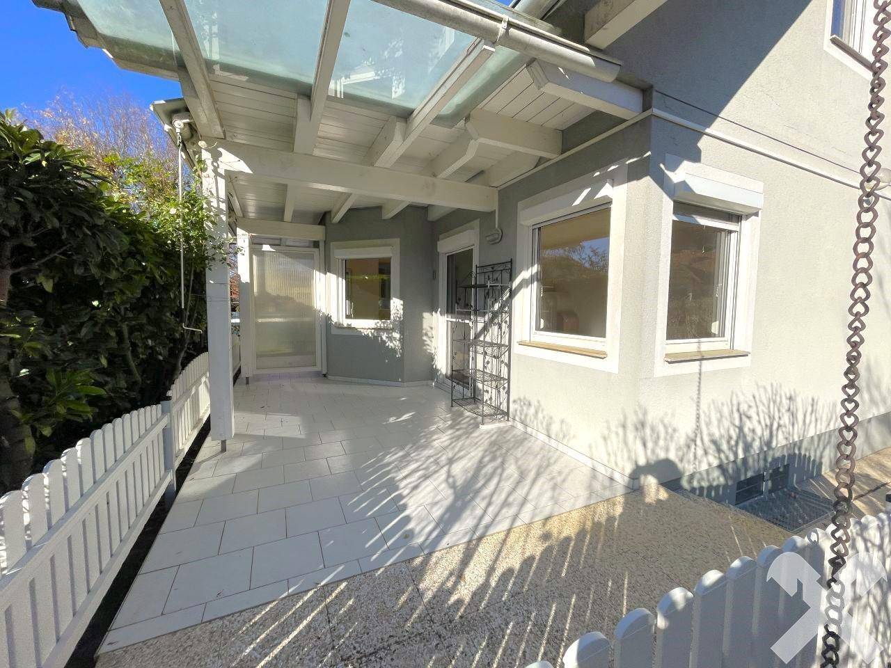 Überdachte Terrasse mit Fliesenboden und weißem Zaun, ideal für entspannte Stunden im Freien.