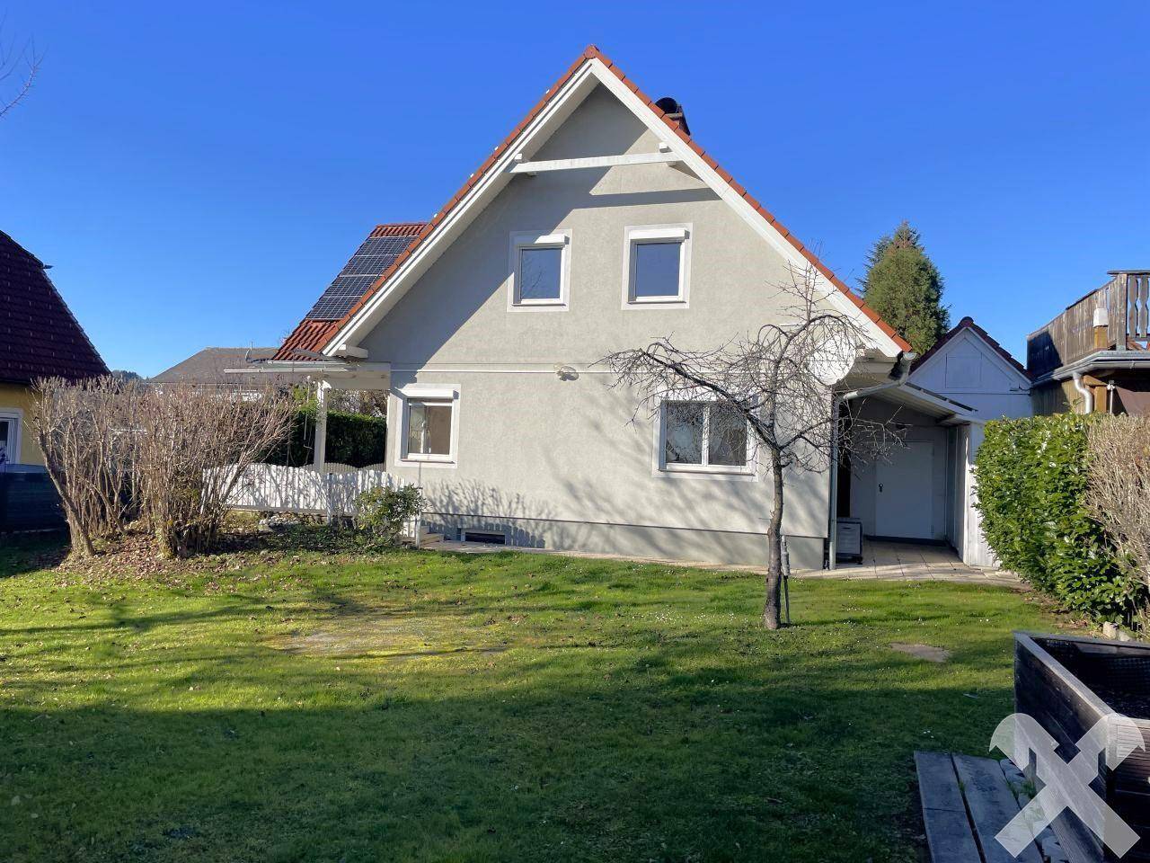 Rückseite des Hauses mit großem, sonnigen Garten und Photovoltaikanlage auf dem Dach.