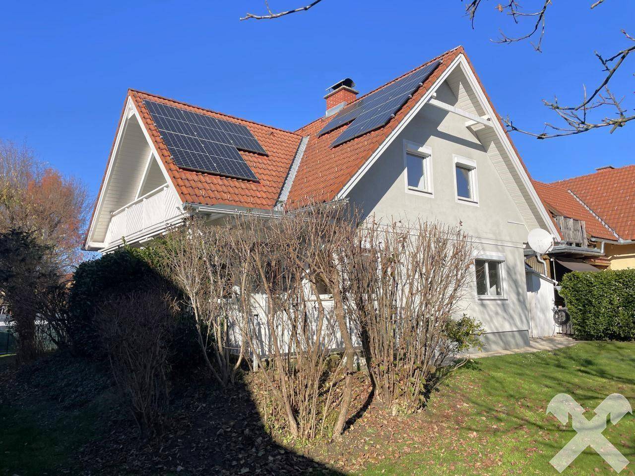 Seitenansicht des Hauses mit Photovoltaikanlage auf dem Dach und umliegender Bepflanzung.