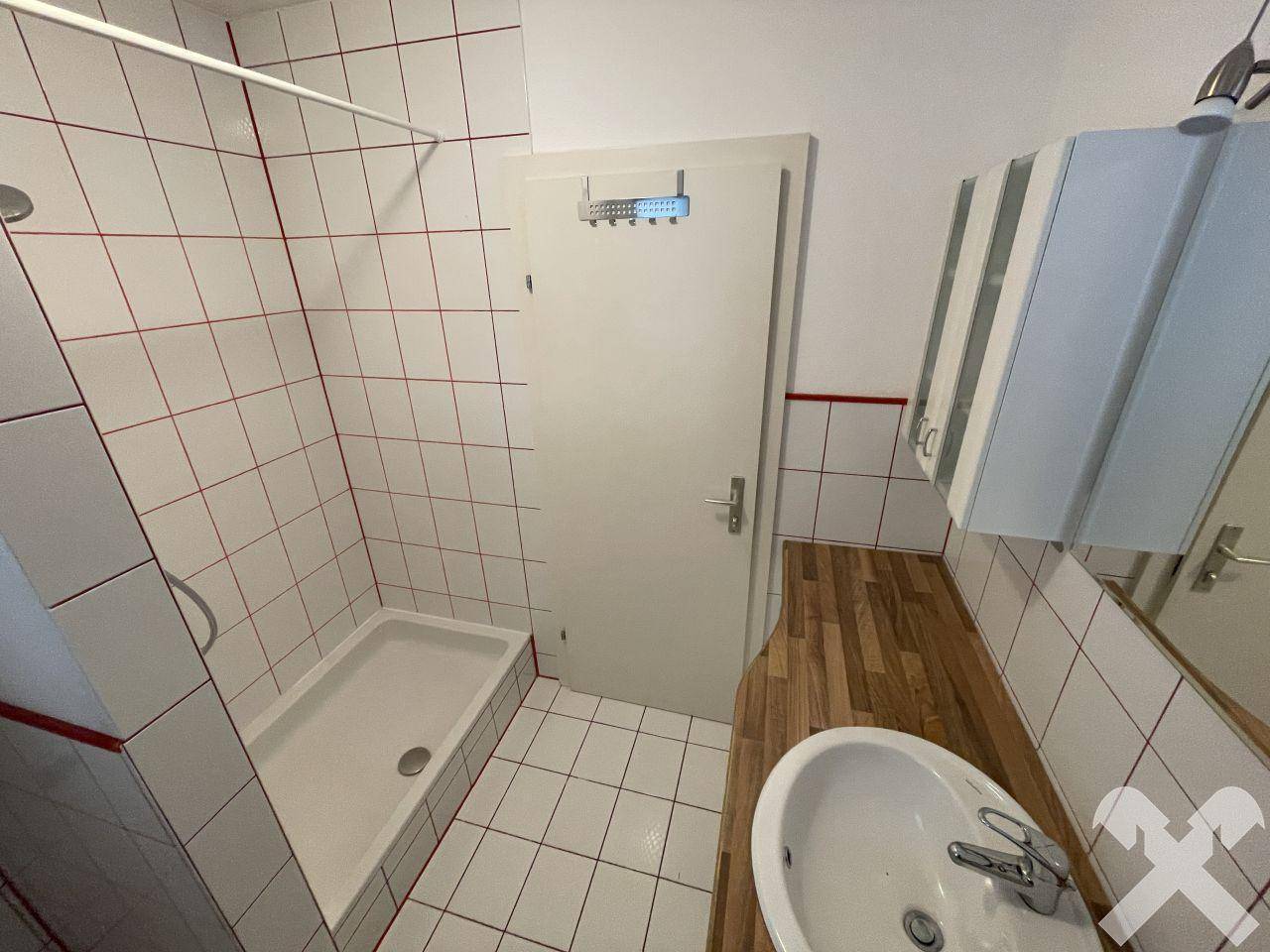 Badezimmer mit Duschkabine, Waschbecken und Holzwaschtisch, hell gefliest.