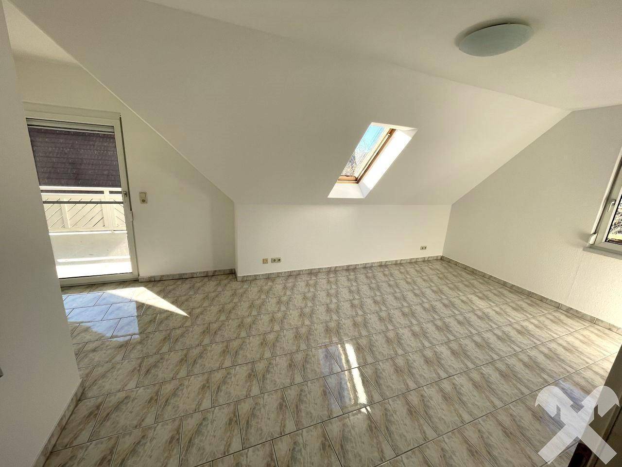 Helles Zimmer im Dachgeschoss mit Fliesenboden, Dachfenster und Zugang zum Balkon.