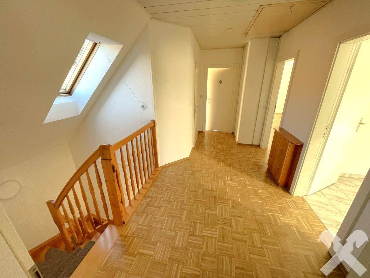Heller Flur im Obergeschoss mit Holztreppe, Parkettboden und Dachfenster.